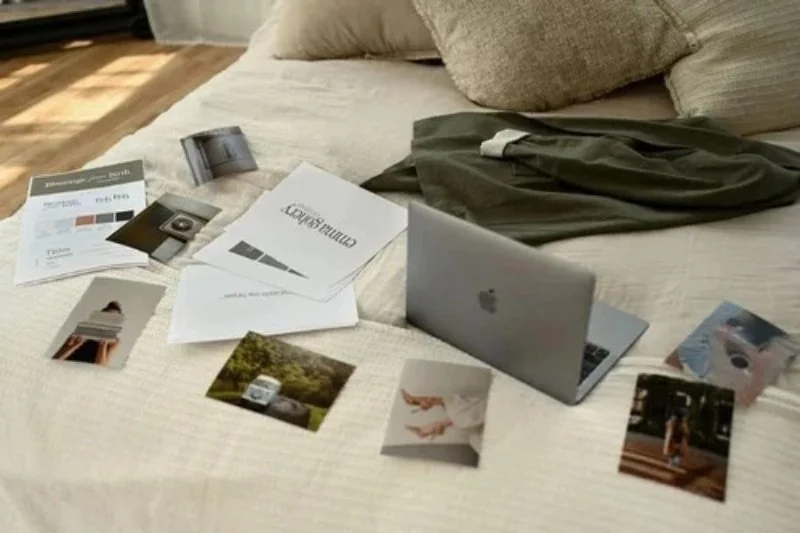 Flat lay of laptop, brand materials, and photos on bed, showing cohesive professional branding and creative workspace