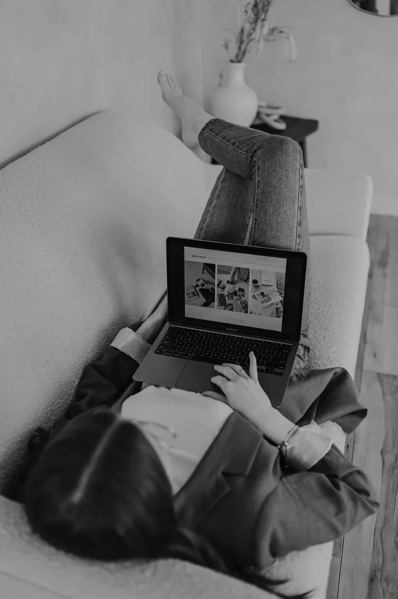 Black and white photo of woman reviewing website strategy on laptop while relaxing on couch.