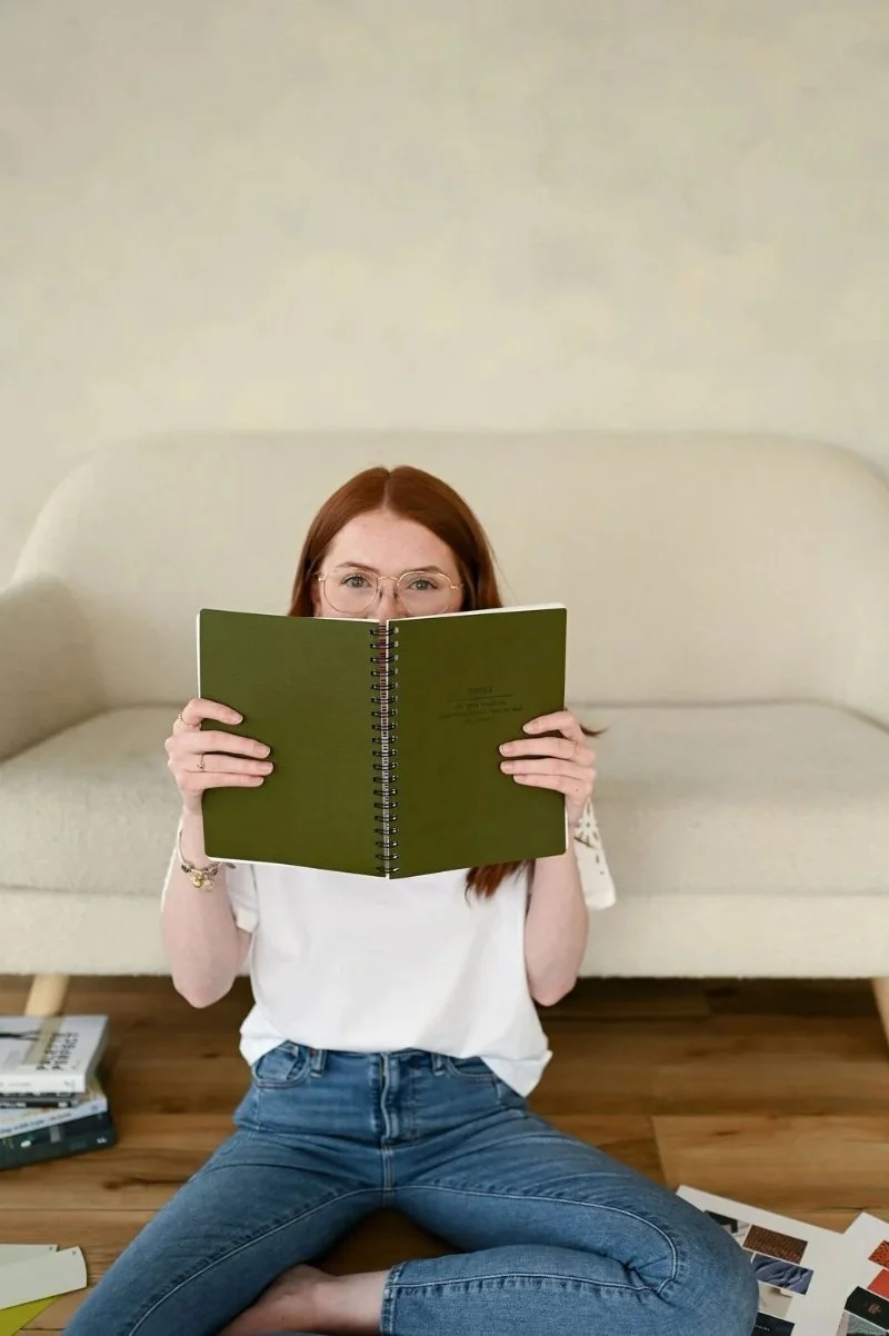 Woman holding notebook in front of face, planning ideas for web design in Edmonton, calm and creative setting.
