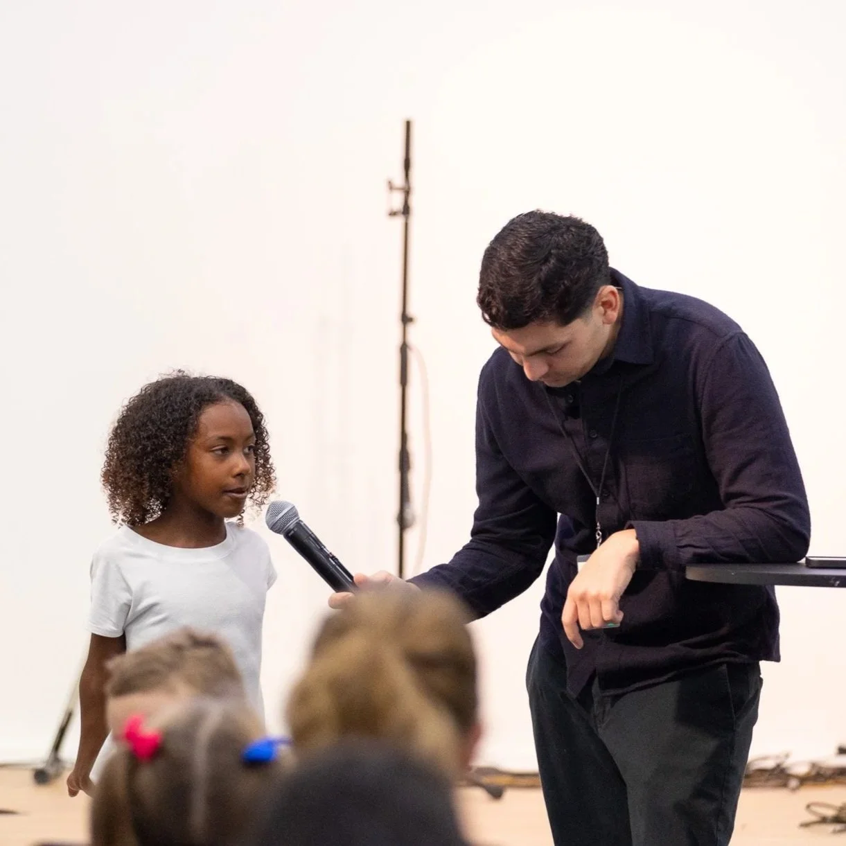Children participating in an indoor activity, raising their hands, many wearing masks.