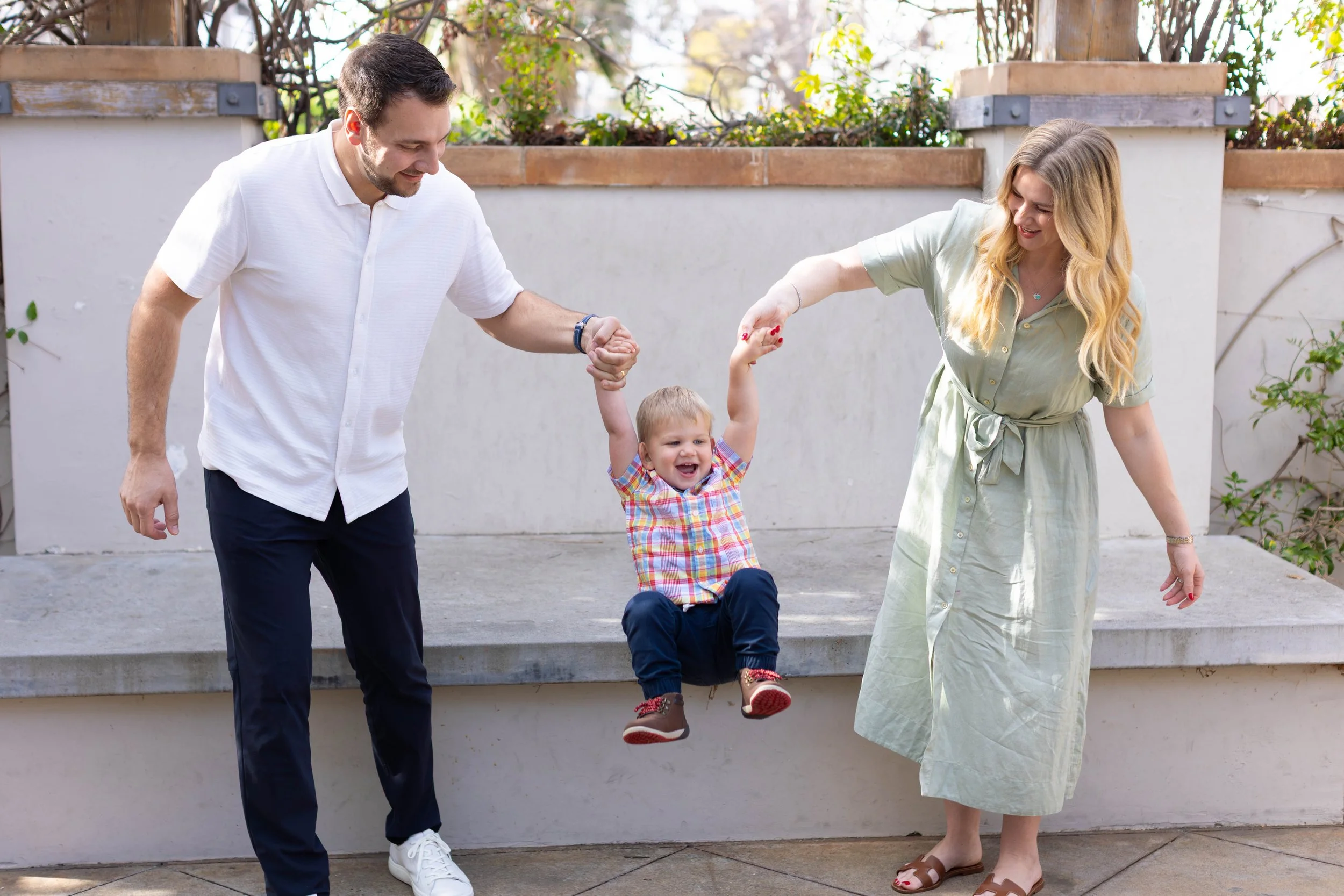 A woman with red hair, sitting on a sofa, holding a young child while another child looks at a tablet.