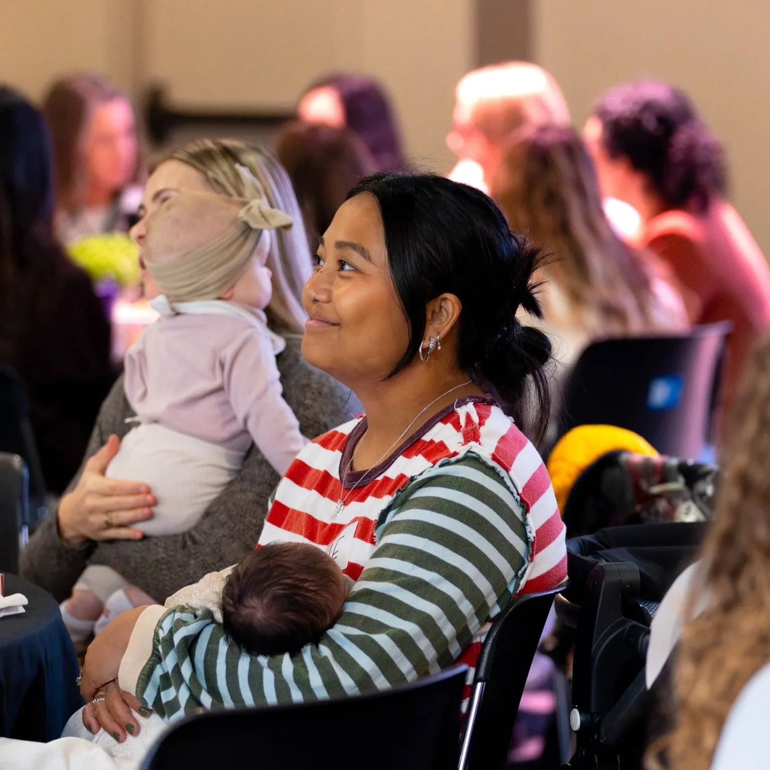 A woman holding a newborn baby close to her chest, in a warmly lit room with a world map on the wall.