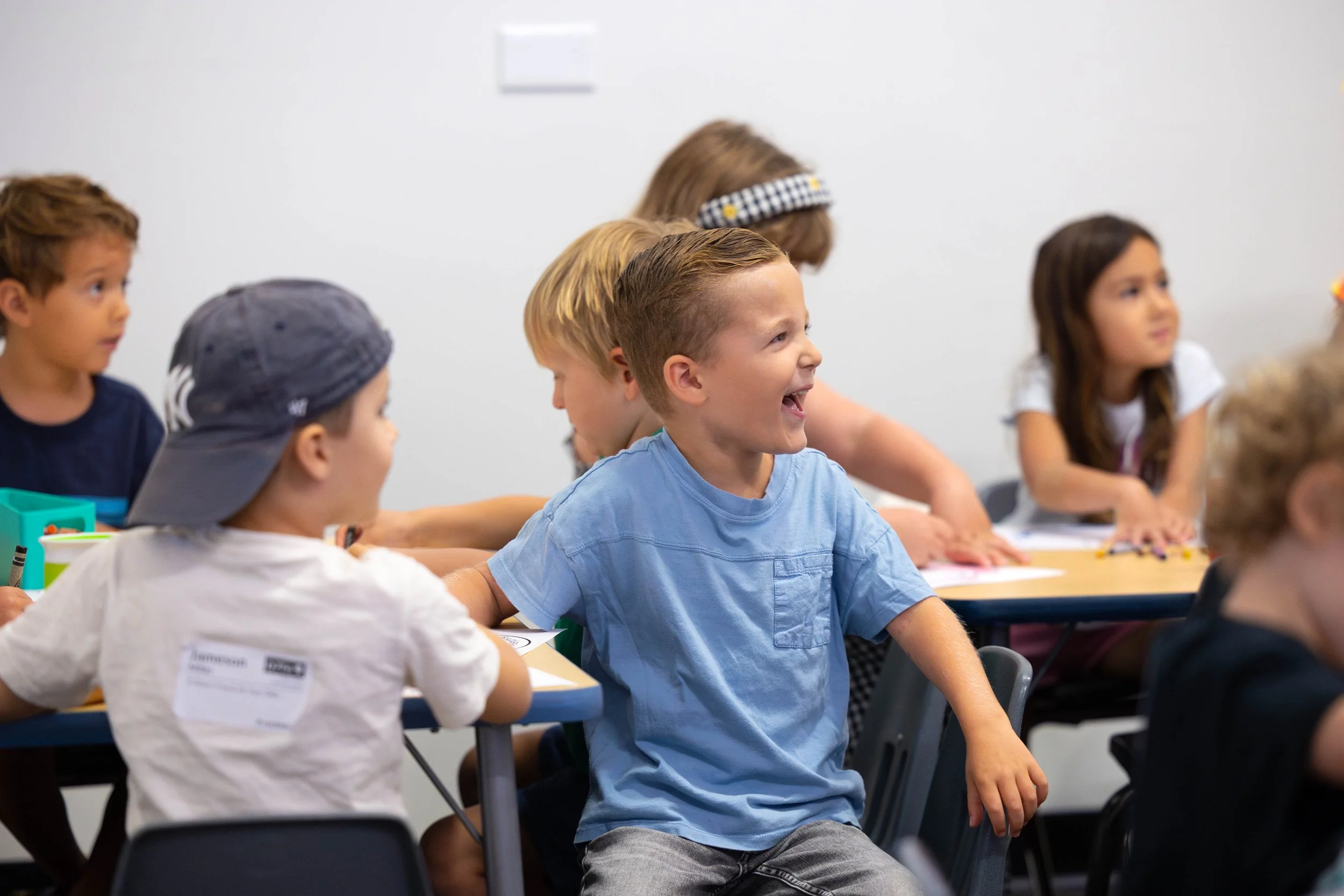 Two young boys, one with brown hair and one with blond hair, are standing and looking at a white grid display with papers attached, in what appears to be an indoor setting.