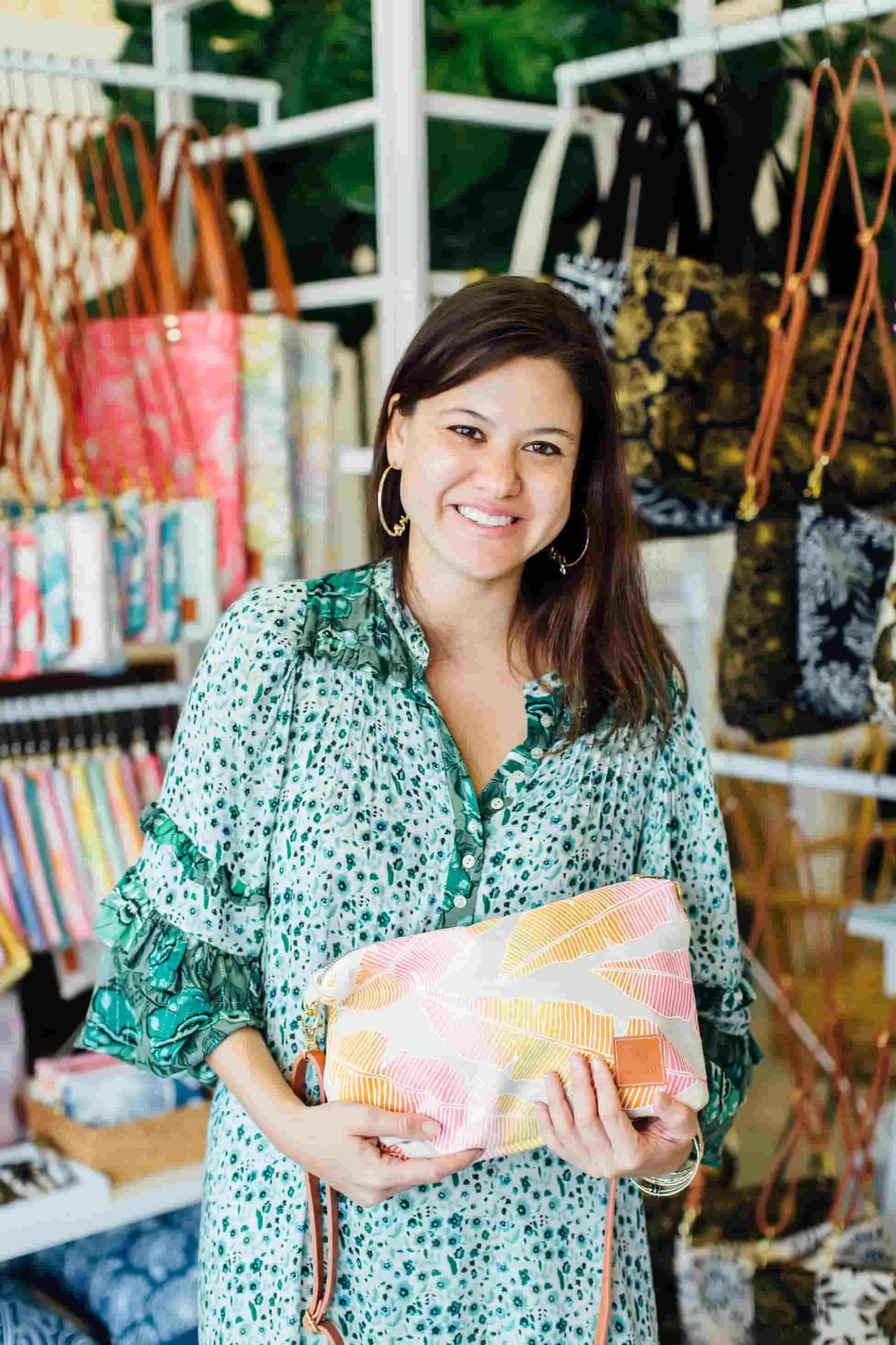 Woman in patterned green top holding a colorful bag in a store with bags displayed on shelves.