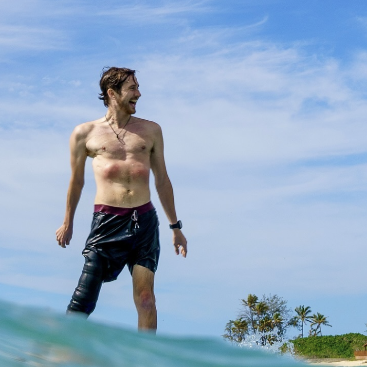 Man in black swim shorts enjoying the beach with tropical greenery in the background.