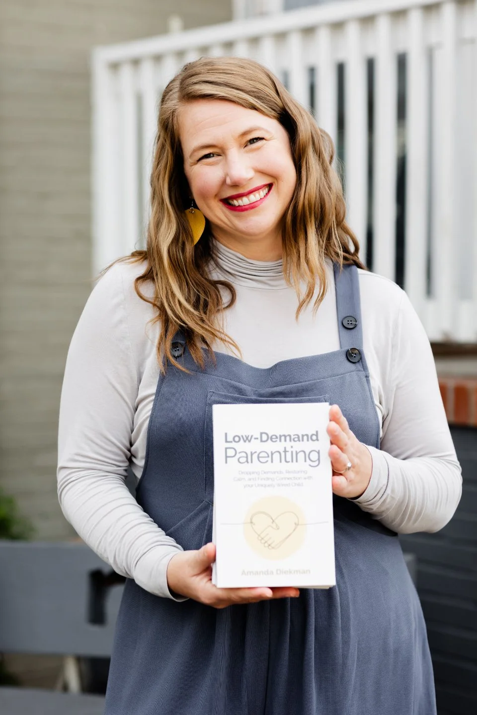 A person smiling and holding a book titled 'Low-Demand Parenting' by Amanda Diekman.