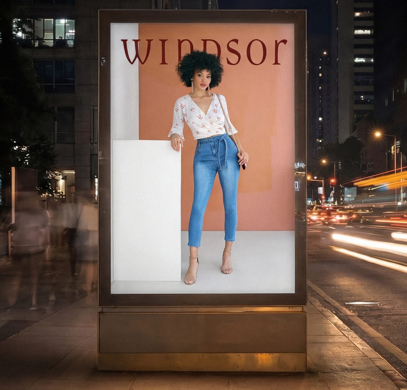 Fashion advertisement showing woman modeling Windsor outfit on illuminated street billboard at night.