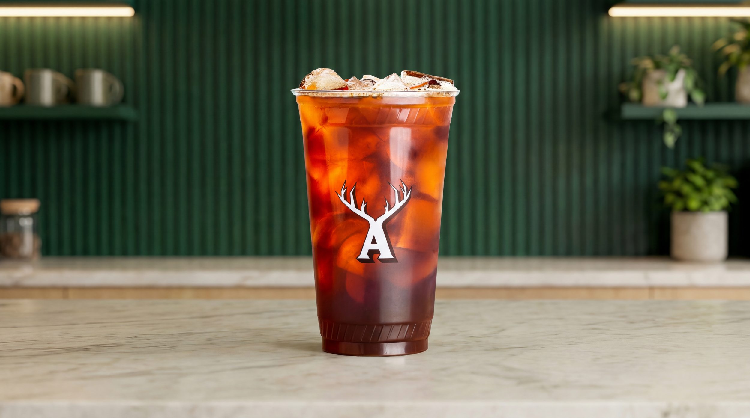 Iced coffee served in clear plastic cup with Alfred Coffee antler logo, filled with ice on countertop.