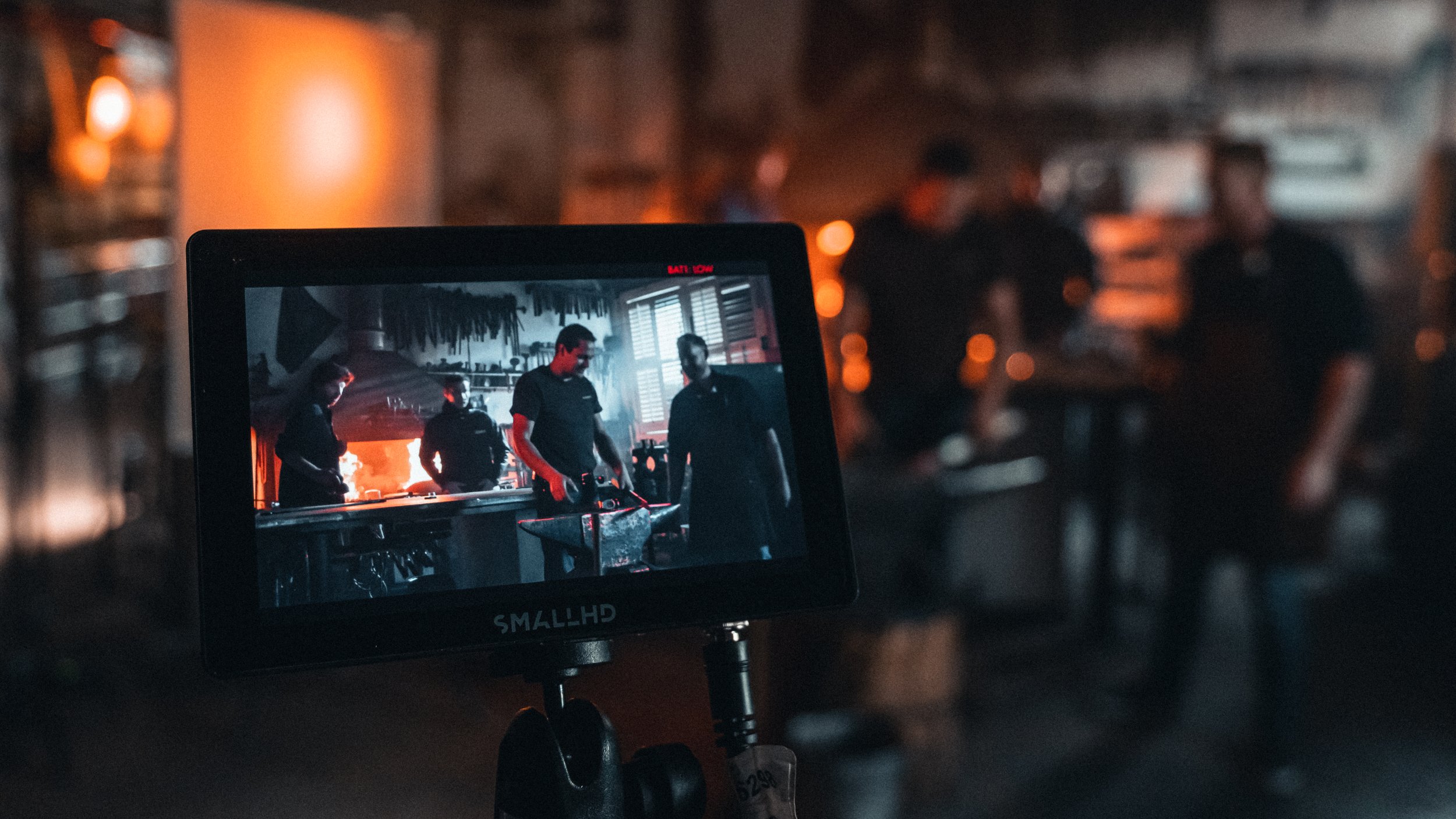 Een camera op een statief neemt een scène op van vier mensen in een keuken, met de scène zichtbaar op het scherm van de camera.