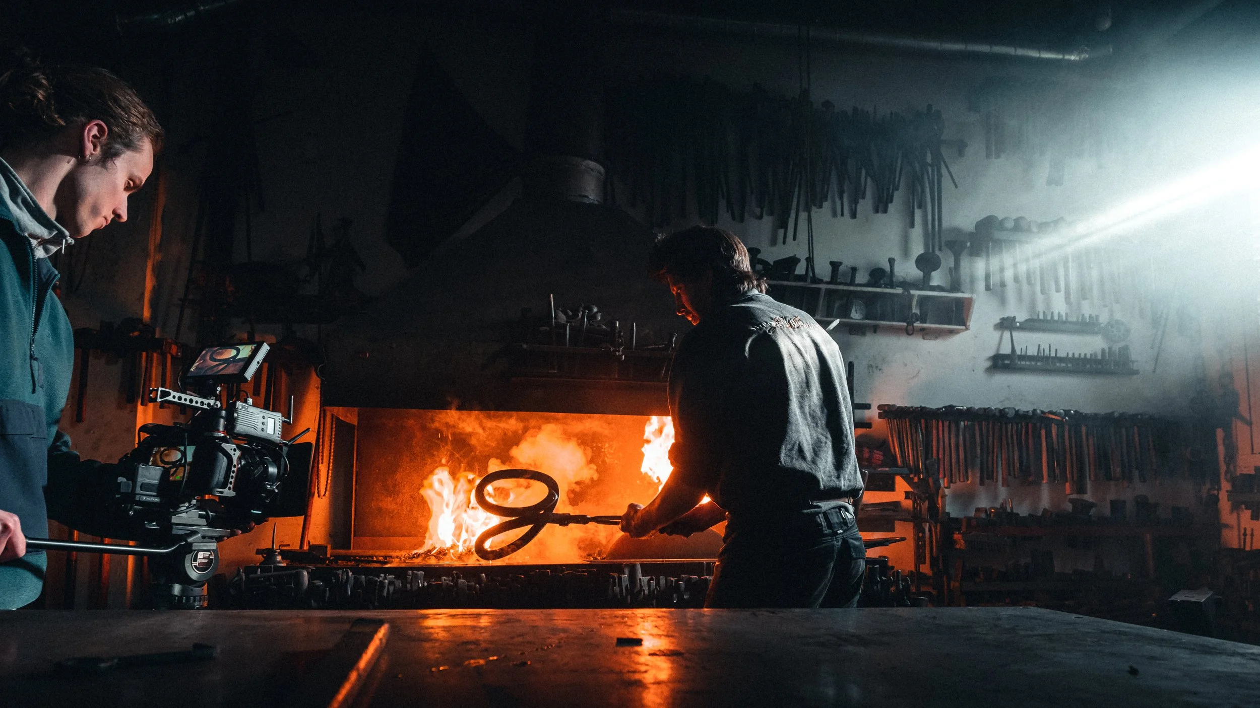 Mensen werken in een blacksmith-werkplaats met vuur en gereedschap, gefilmd door een cameraman.