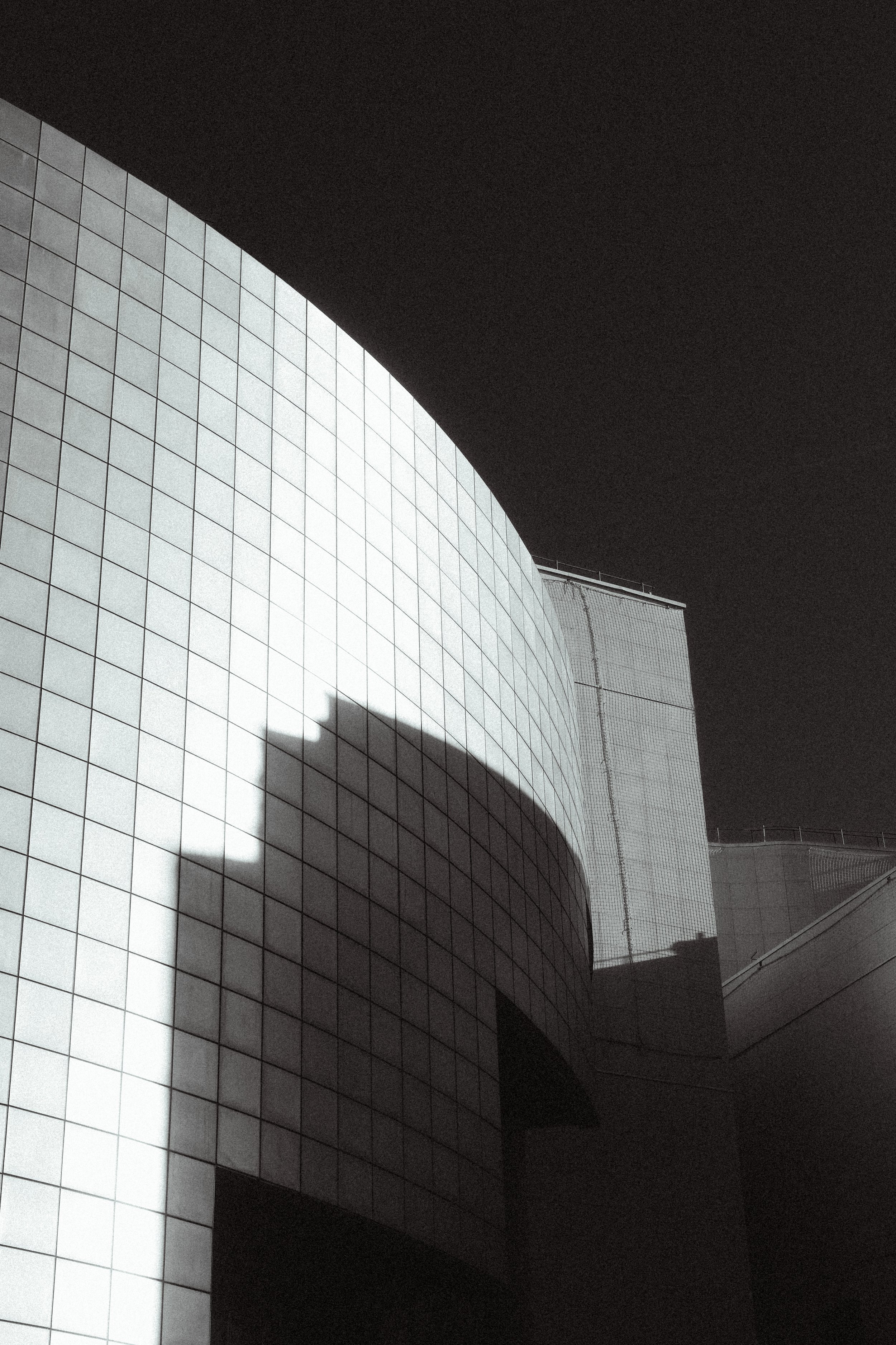 Modern gebouw met een rond, wit betegeld façade en een donkere, onduidelijke achtergrond, mogelijk een nachtbeeld.