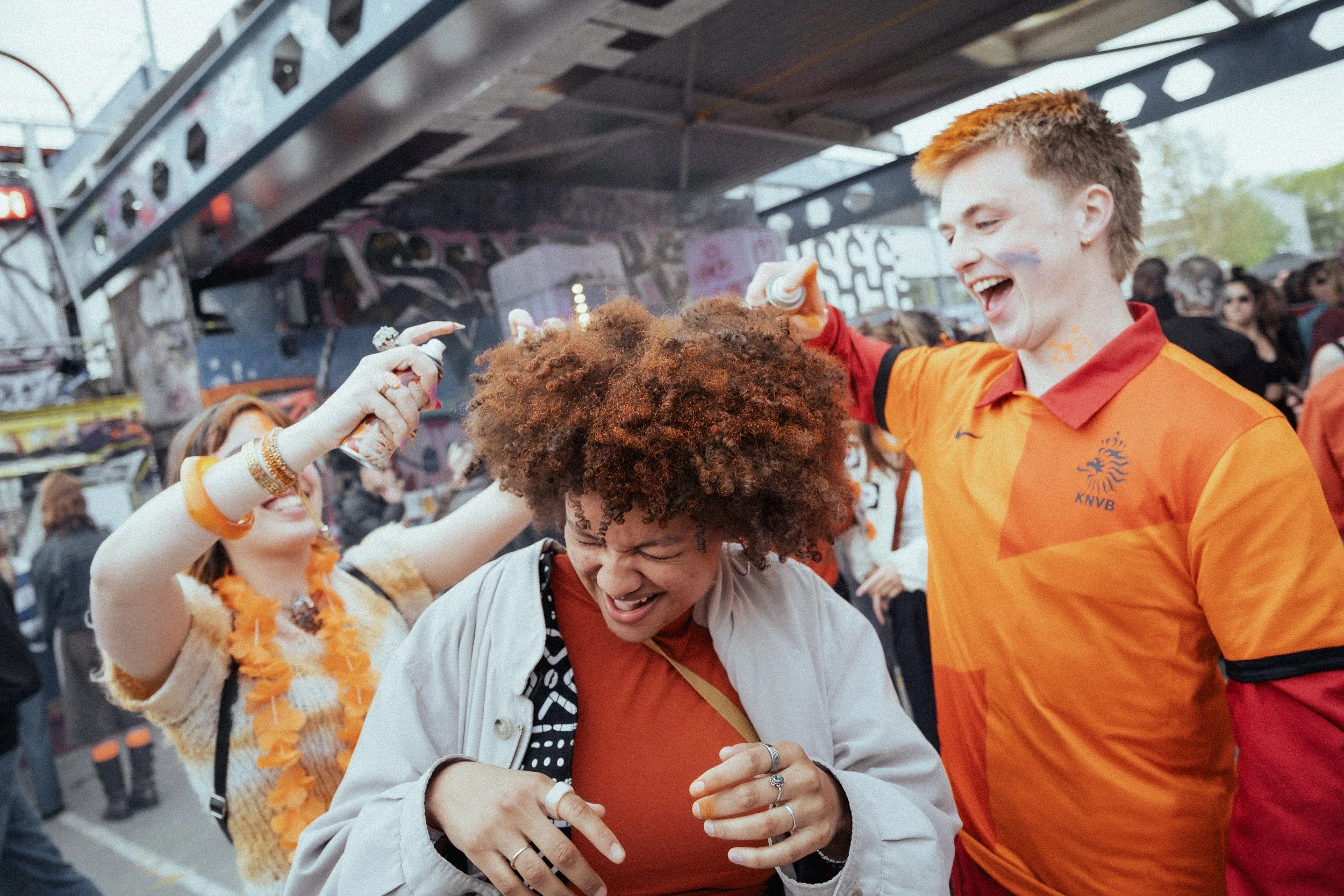 Vrolijke mensen dansen en lachen tijdens een feest of muziekfestival, gekleed in oranje en met feestdecoraties.