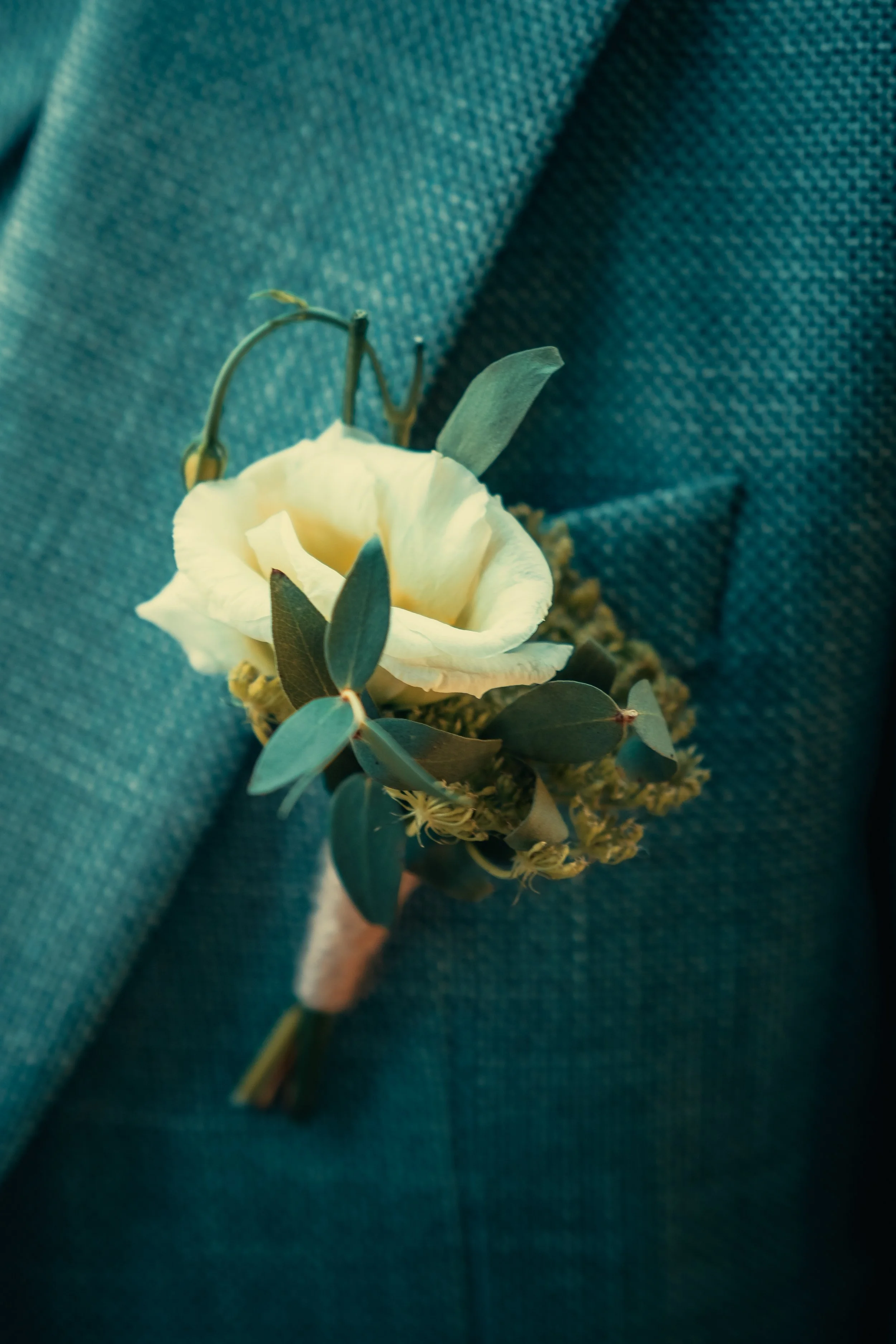 Witte bloem met groene bladeren, bevestigd aan een blauwe, textured stof achtergrond.
