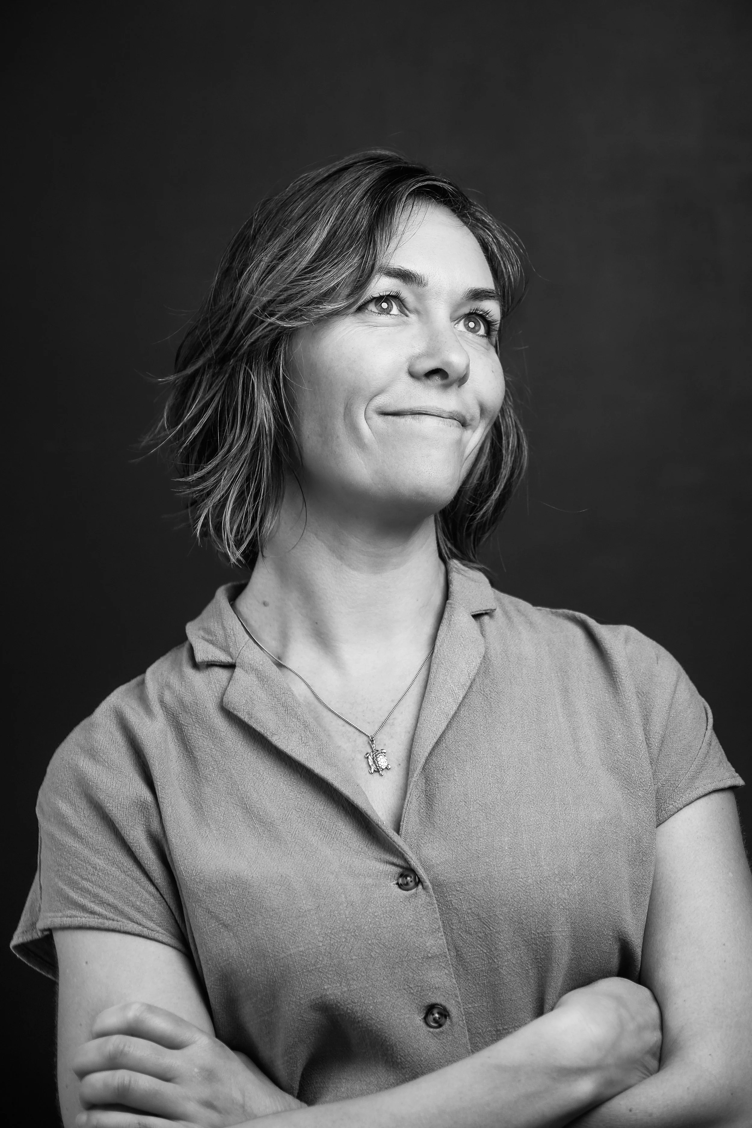 Zwart-wit foto van een vrouw met schouderlange haar, gekleed in een button-up shirt, glimlachend met haar armen gekruist.