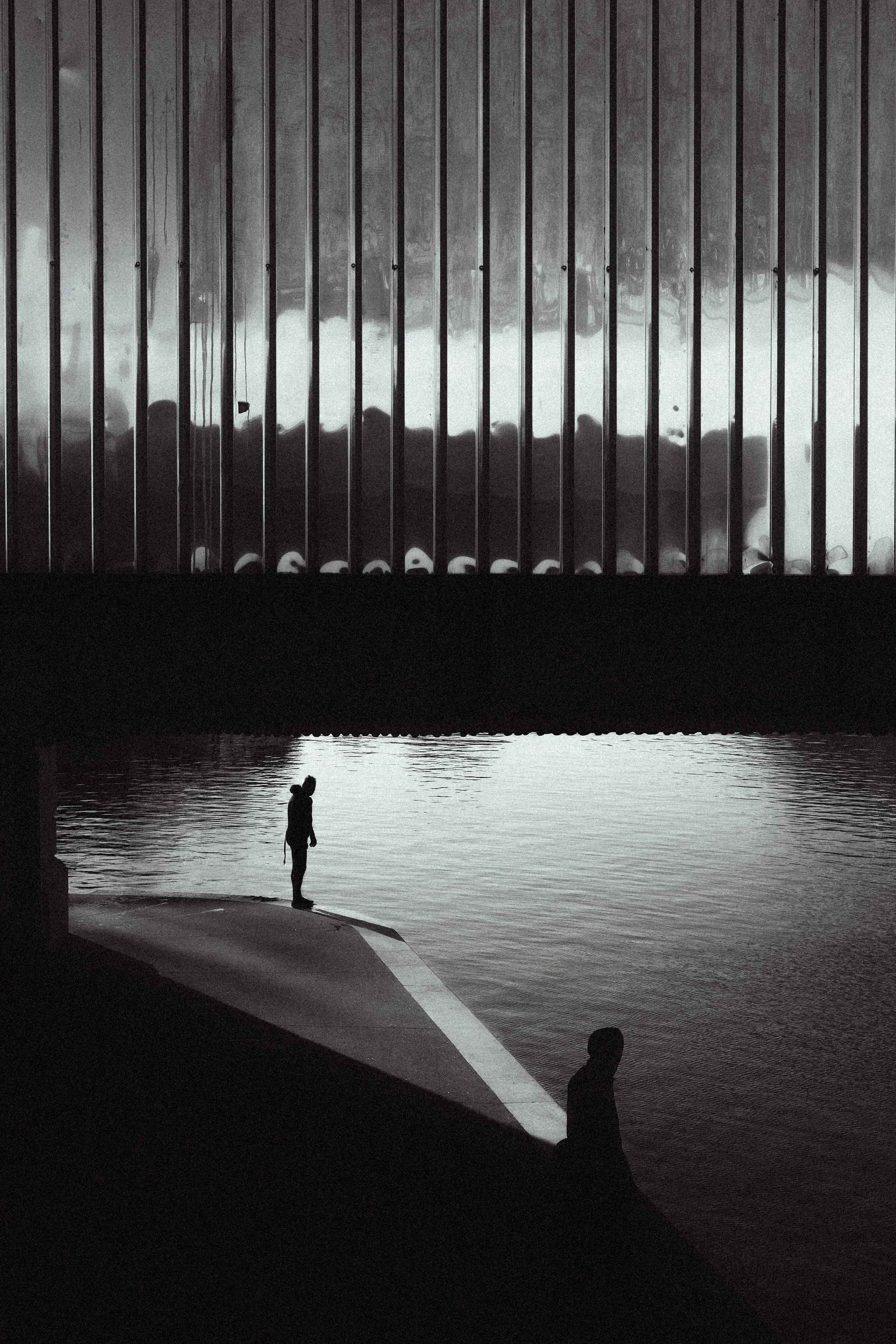 Een zwart-witte foto van een vrouw die door een water onder een brug loopt.