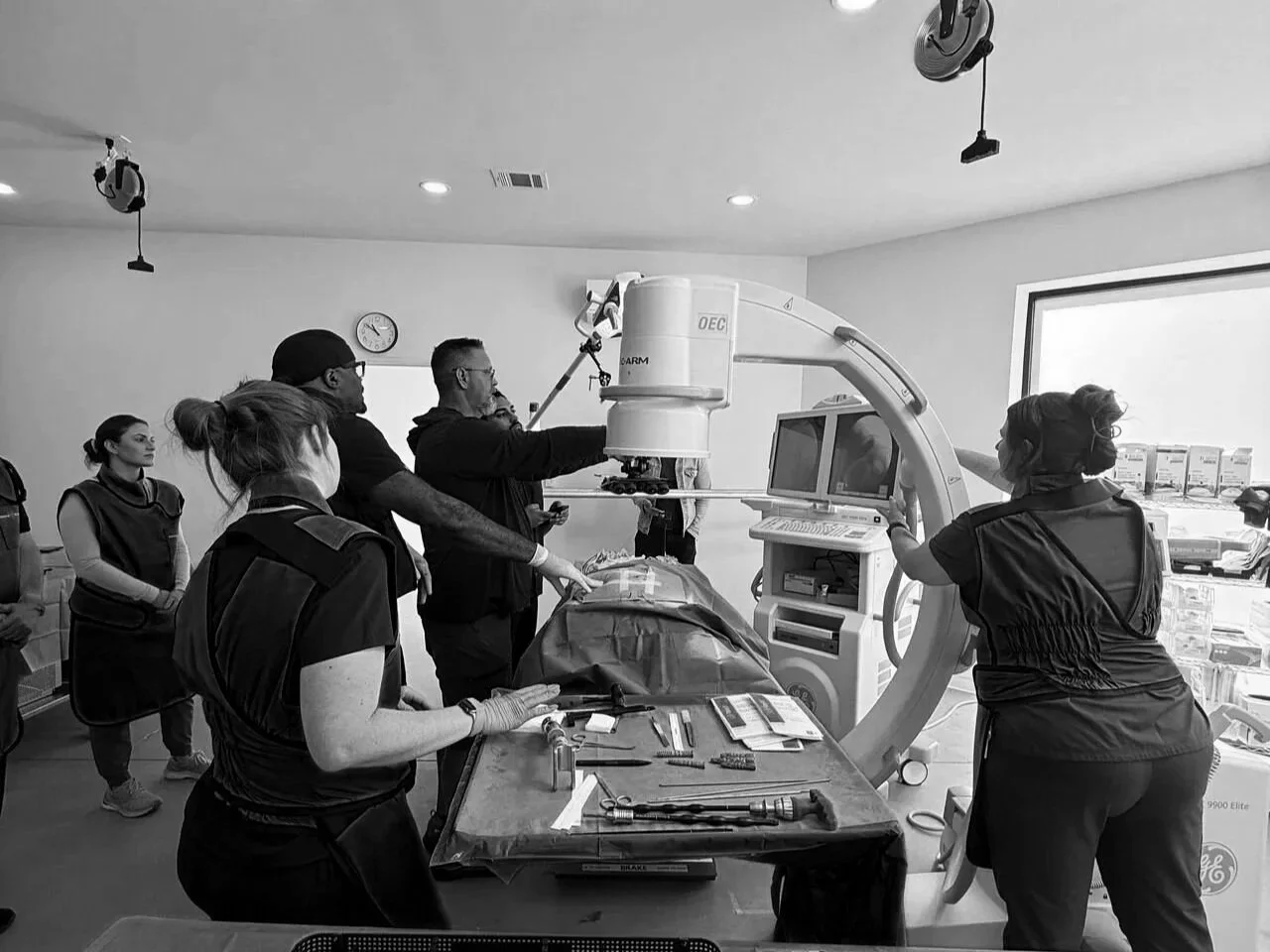 Medical professionals in a hospital room operating a C-arm imaging device for a surgical procedure.