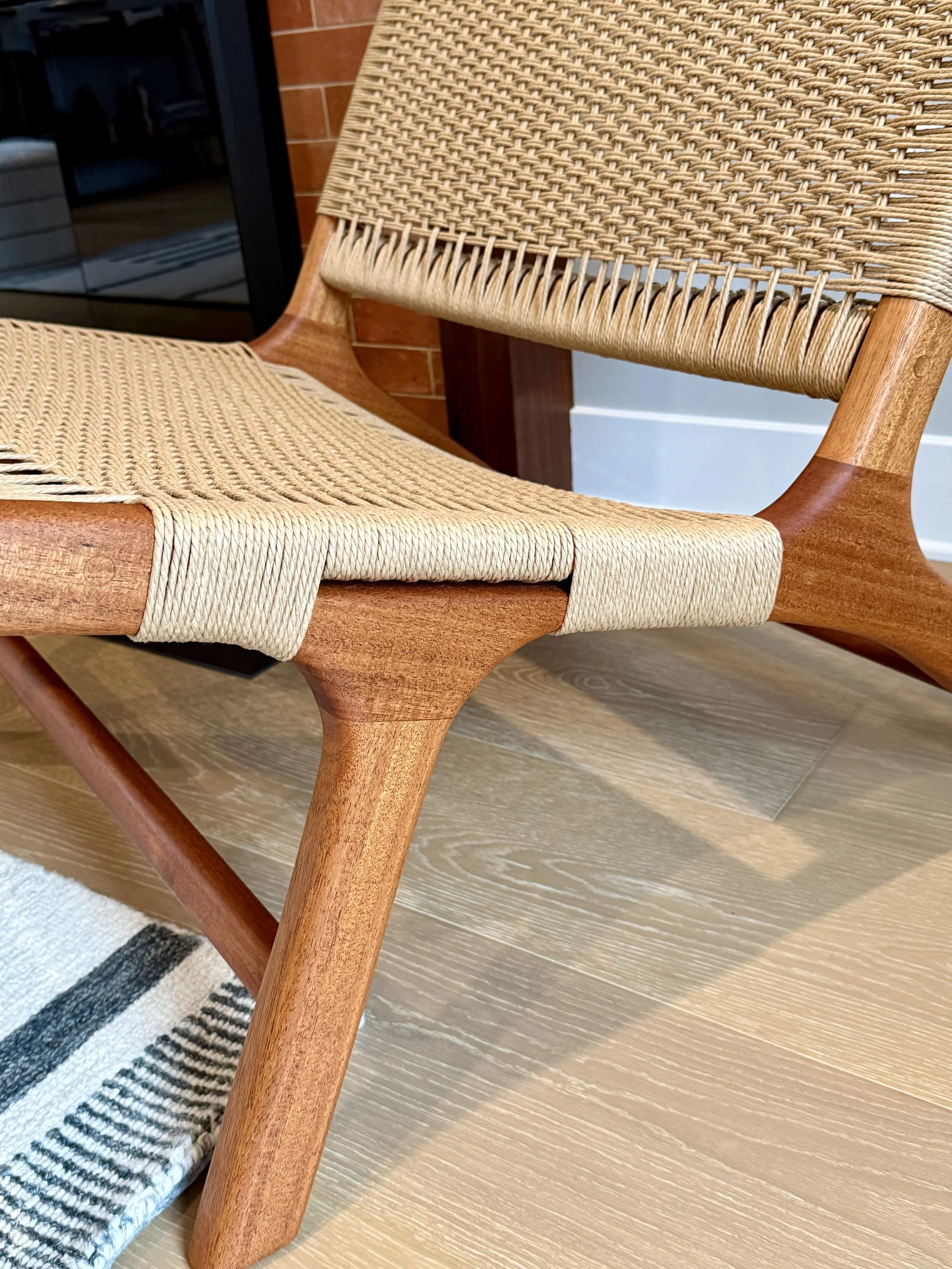Close-up of a wooden chair with danish cord seat and backrest on a light wood floor.