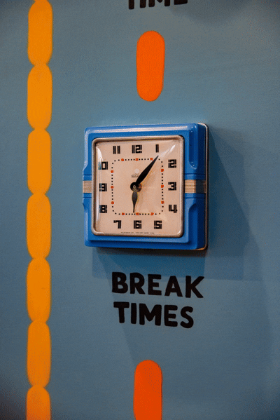 blue french clock hung on a blue wall with playfully spinning hands and a label beneath saying break time