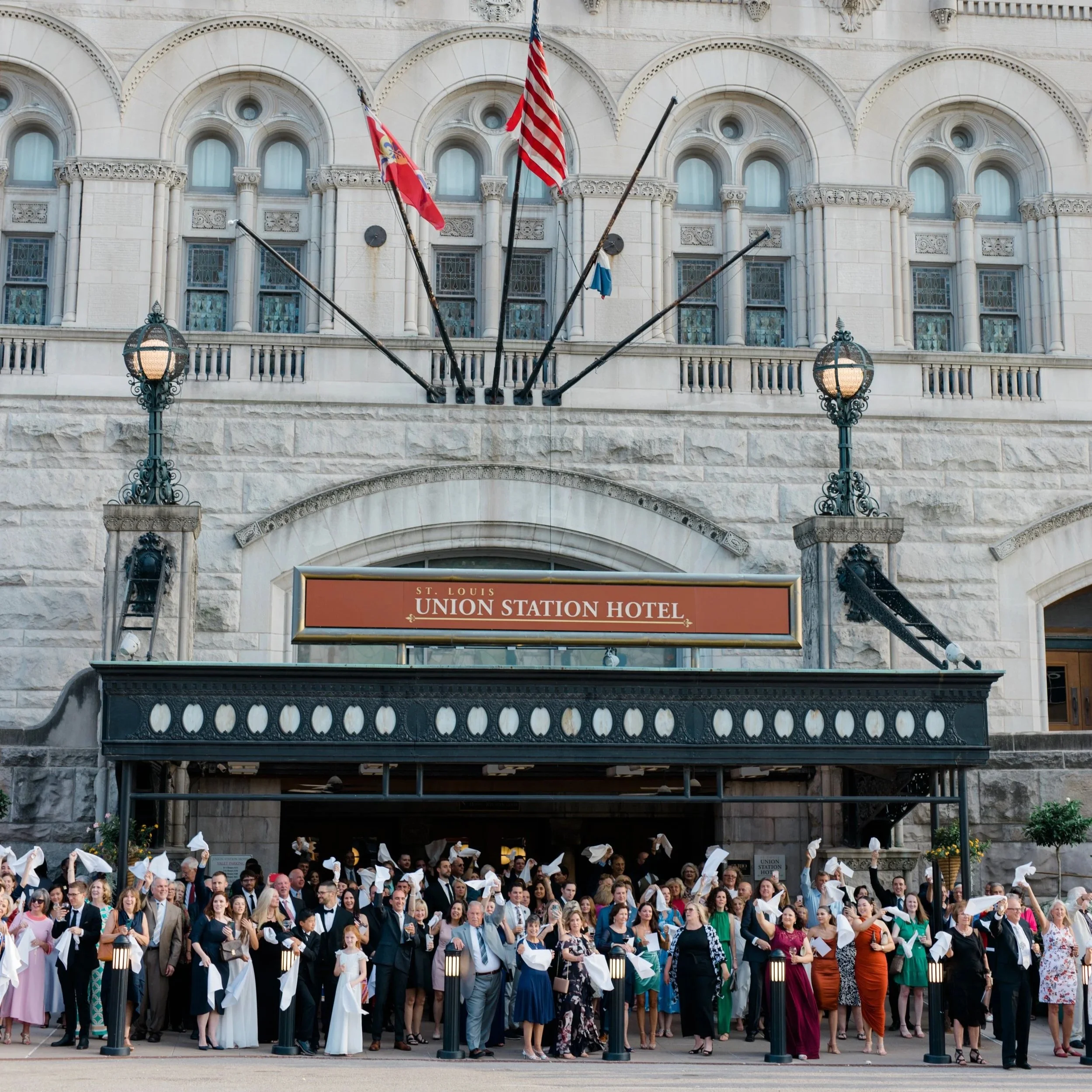 A large group of people in formal attire celebrating outside the Union Station Hotel in St. Louis, holding white napkins in the air.