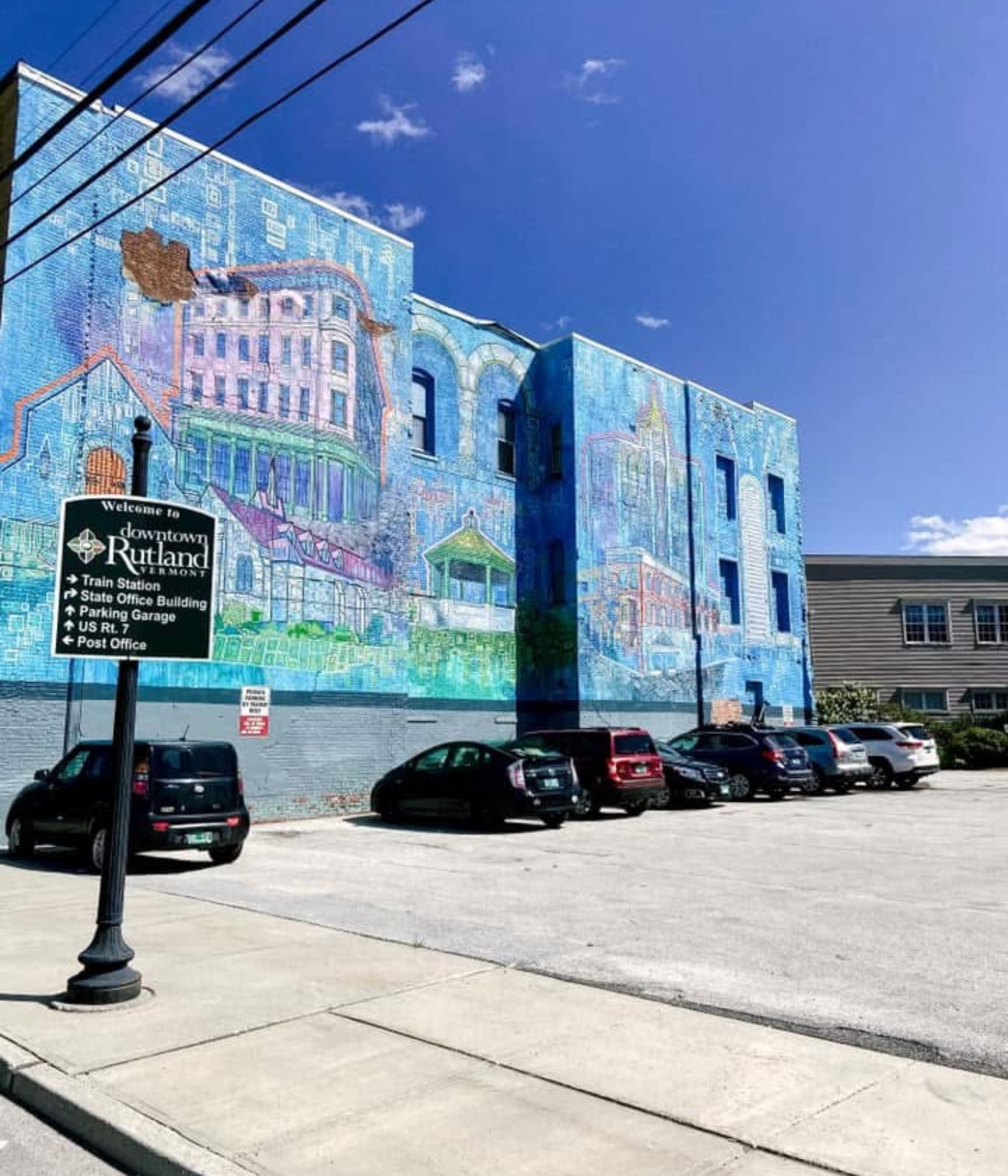 A view of the downtown mural showing farms, a church, and townspeople, painted across the side of a weathered Vermont building.