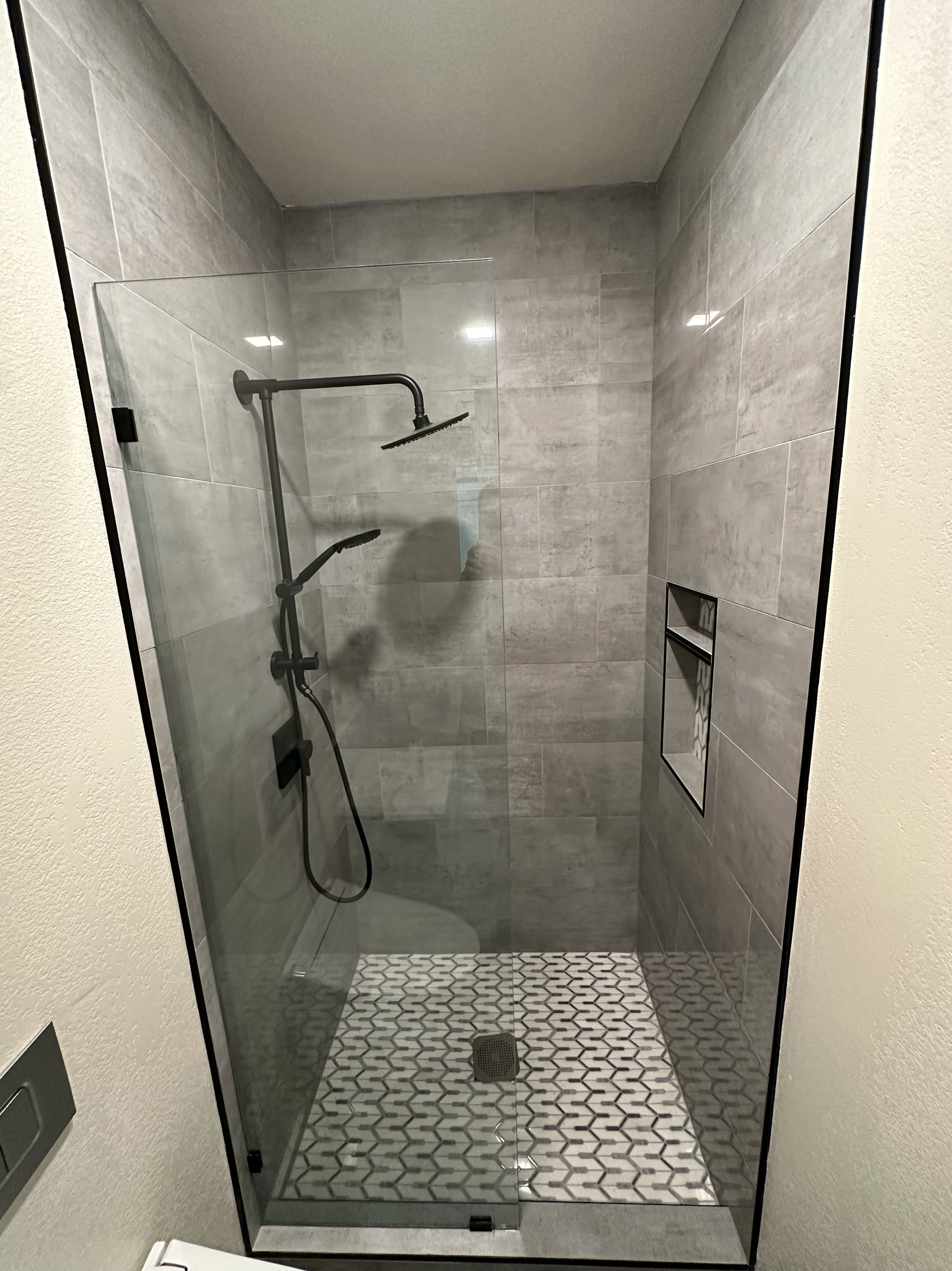 Modern shower with glass door, gray tiles, and rain shower head.