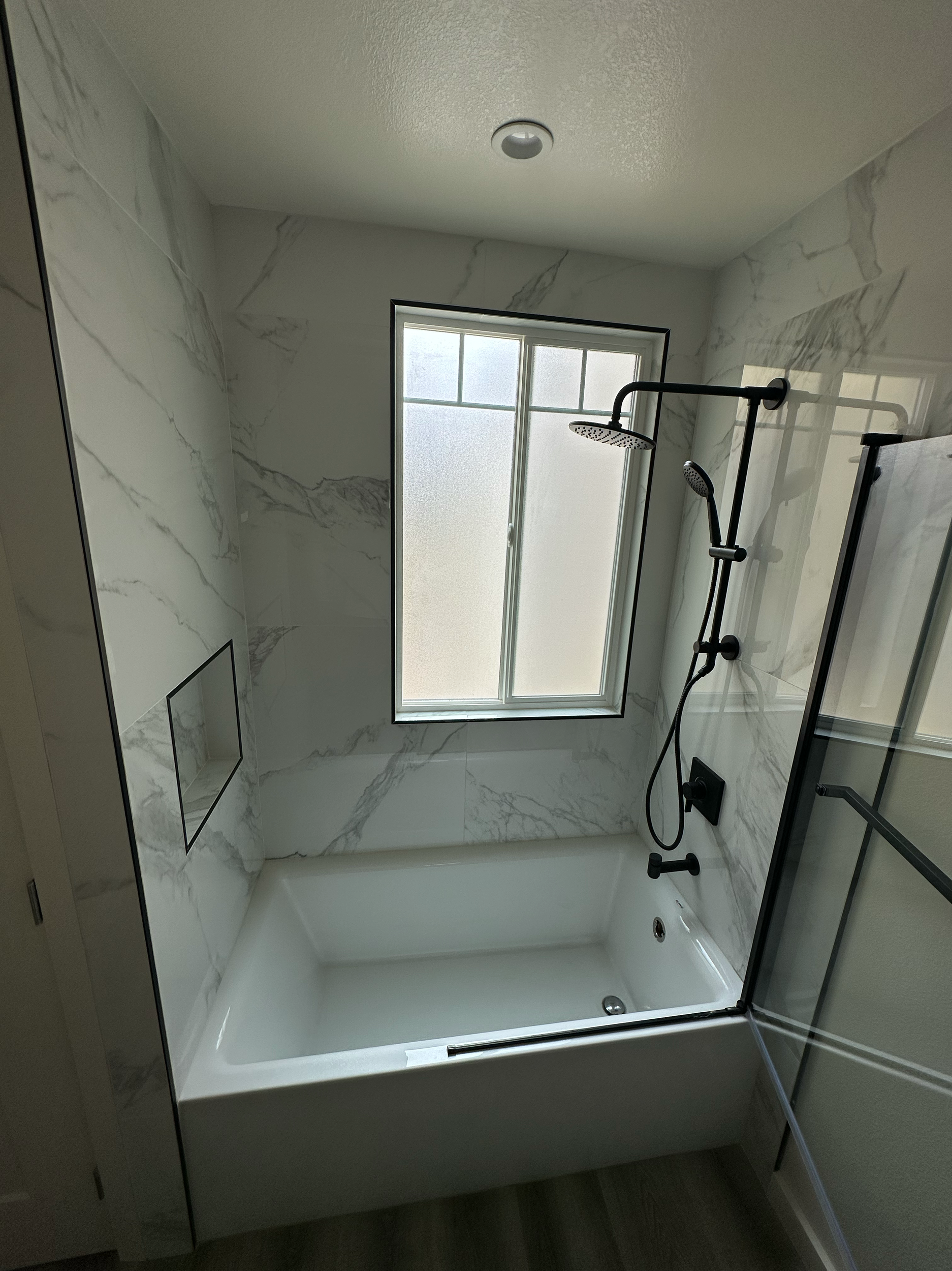 Modern bathroom with marble tile, shower, and frosted window.
