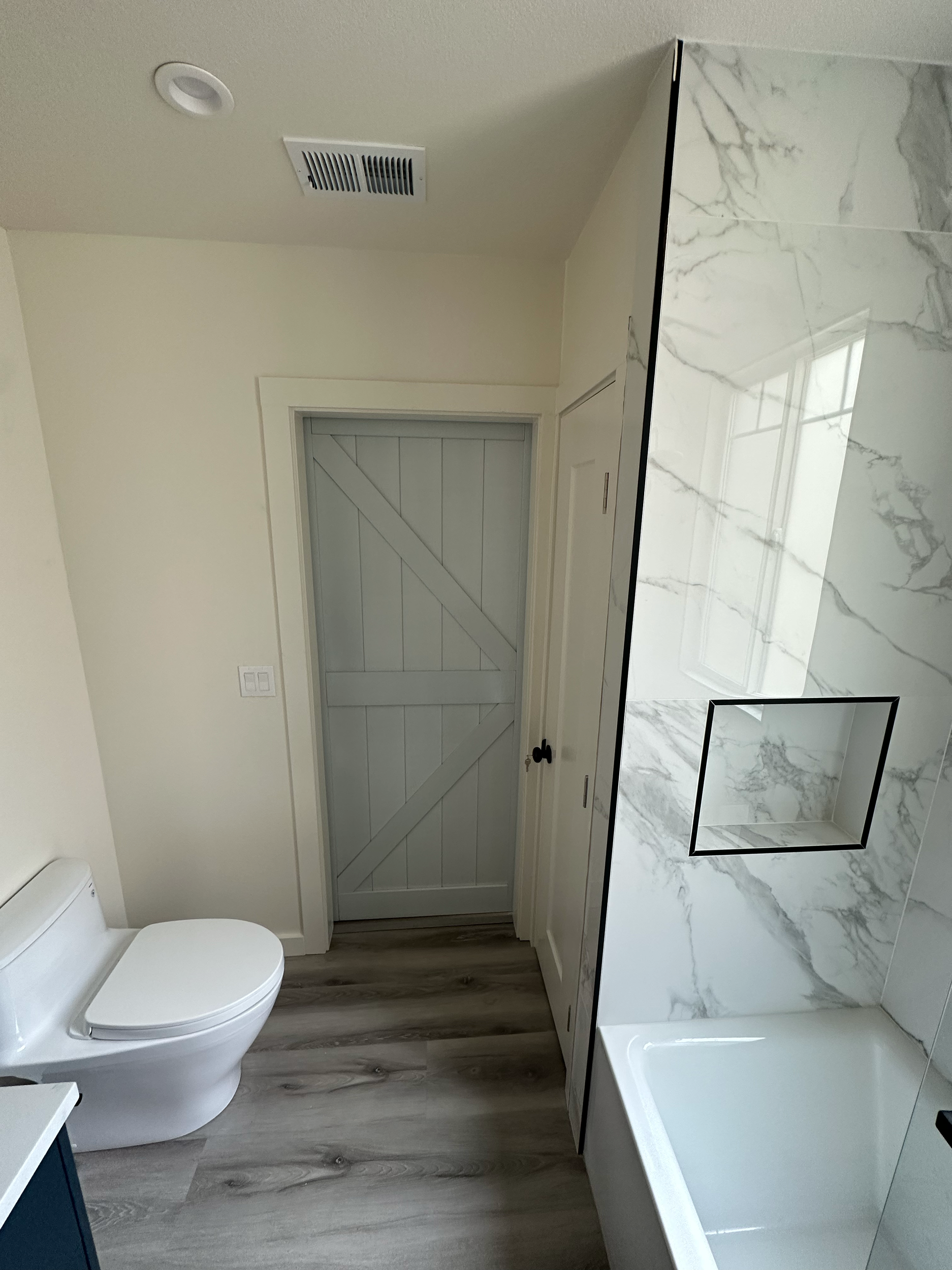 Bathroom with a modern design, featuring a white toilet, marble wall tiles, wooden floor, and a window with slatted shutters.
