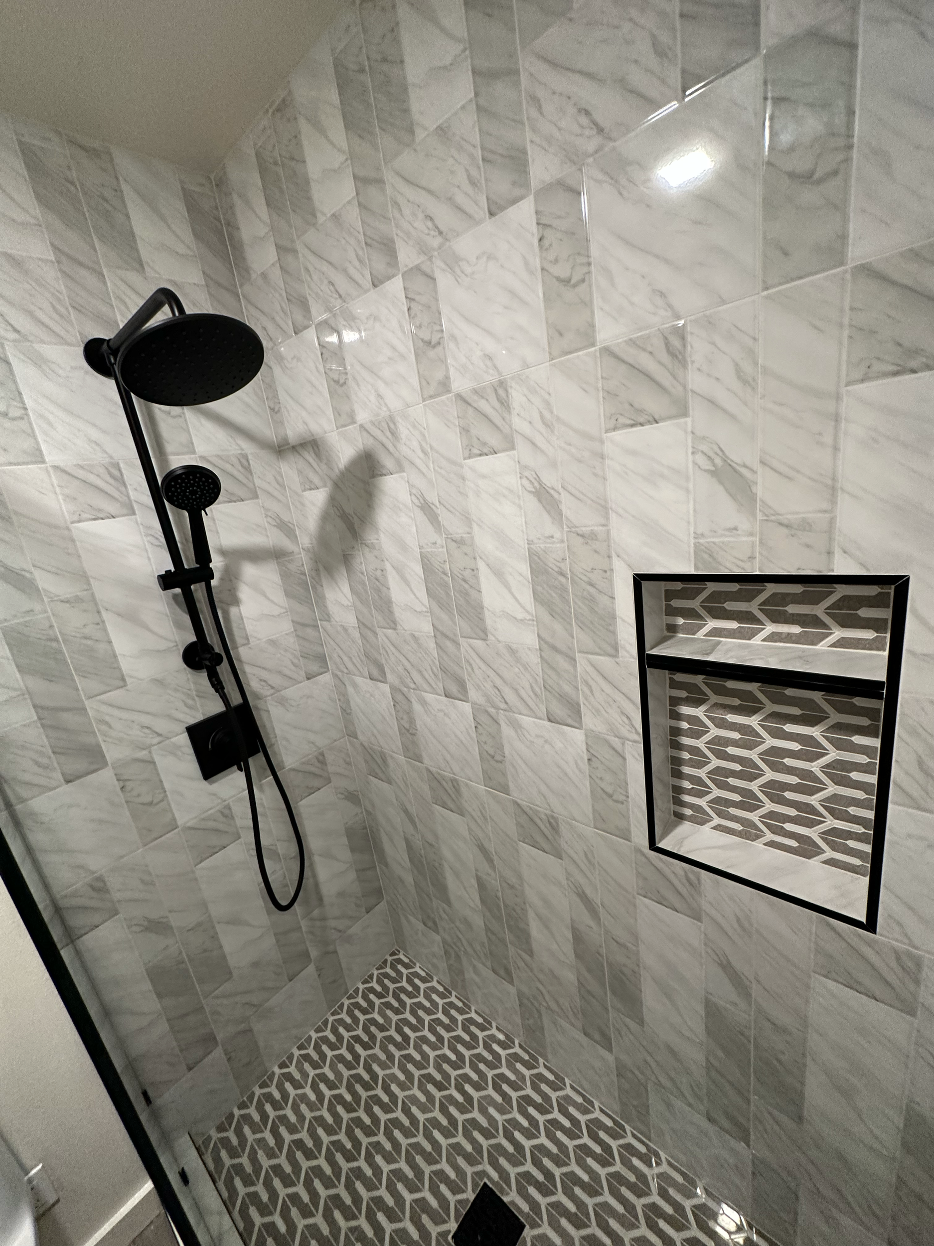 Modern shower area with marble tile walls, black showerhead, and geometric accent pattern.