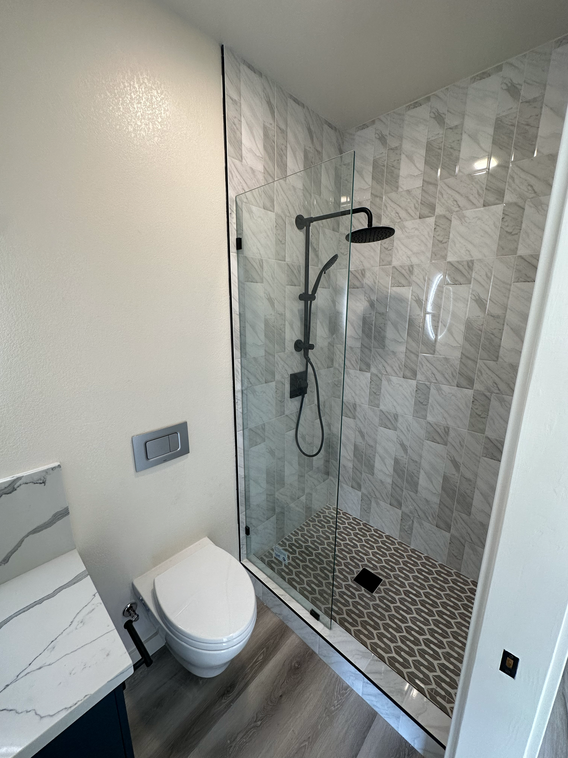 Modern bathroom with glass shower enclosure, marble tile, toilet, and sink with marble countertop.