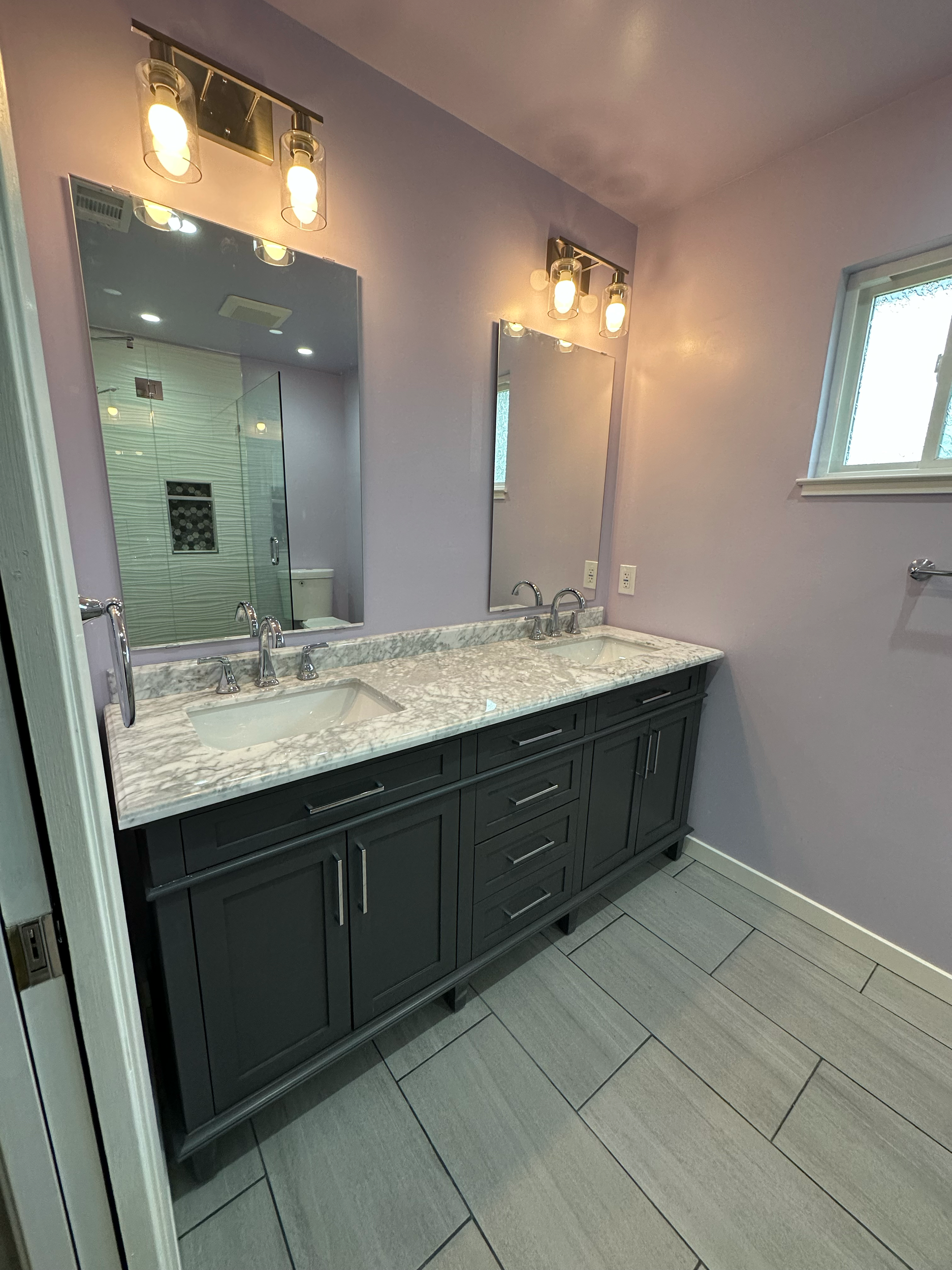 Modern bathroom with gray cabinets, marble countertop, large mirror, and purple walls.