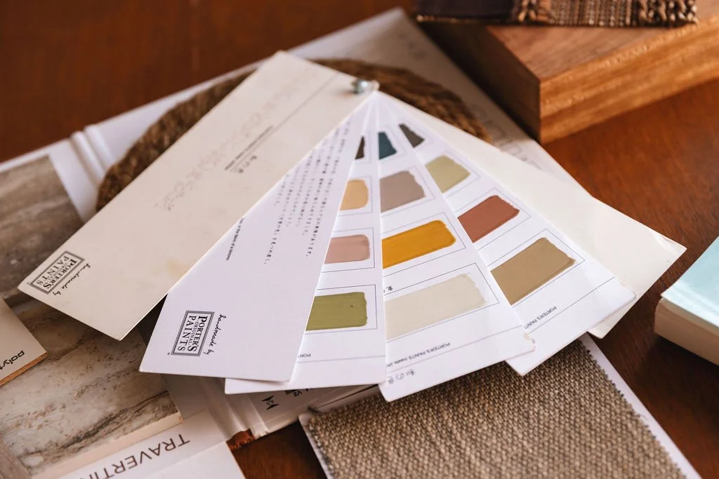 Porters Paints sample fan deck with various paint colors, placed on a wooden surface along with paint swatches and paper samples.