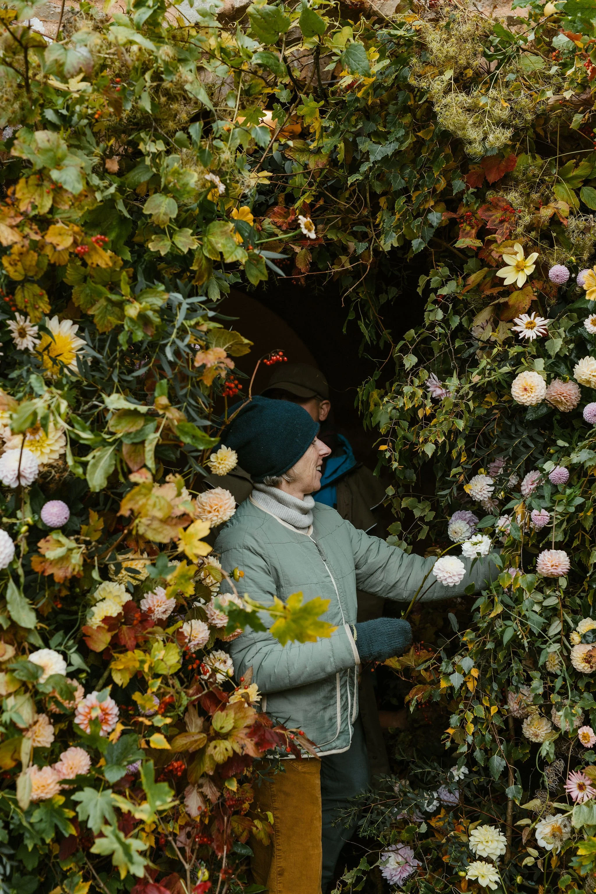 People exploring a tunnel surrounded by lush and colorful fall foliage, including flowers and leaves.