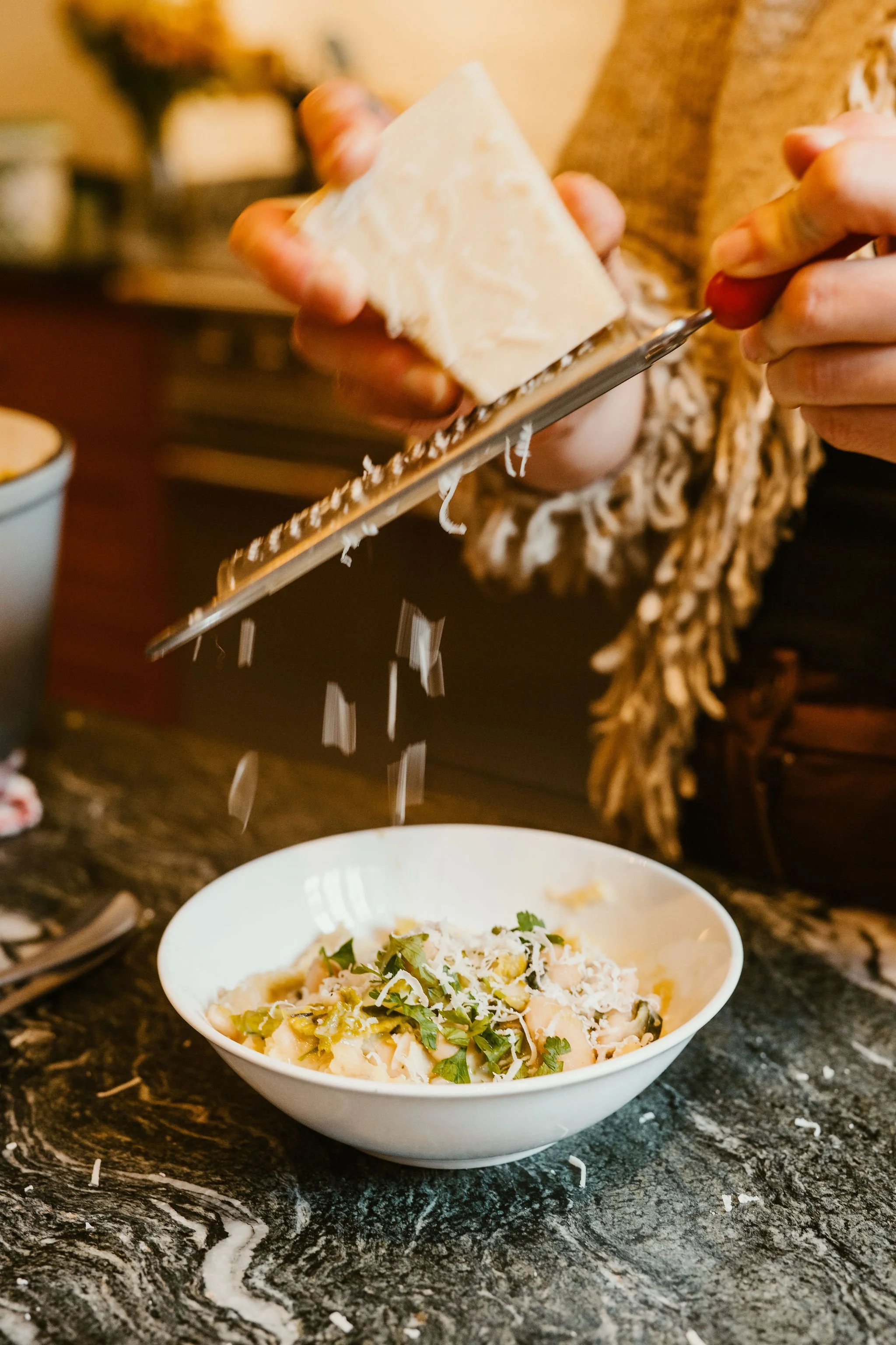 Person grating cheese over a bowl of pasta on a dark marble countertop.