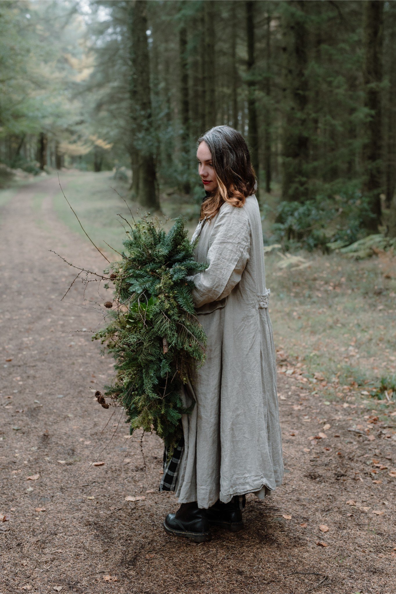 Woman holding a large bouquet of greenery on a forest trail.