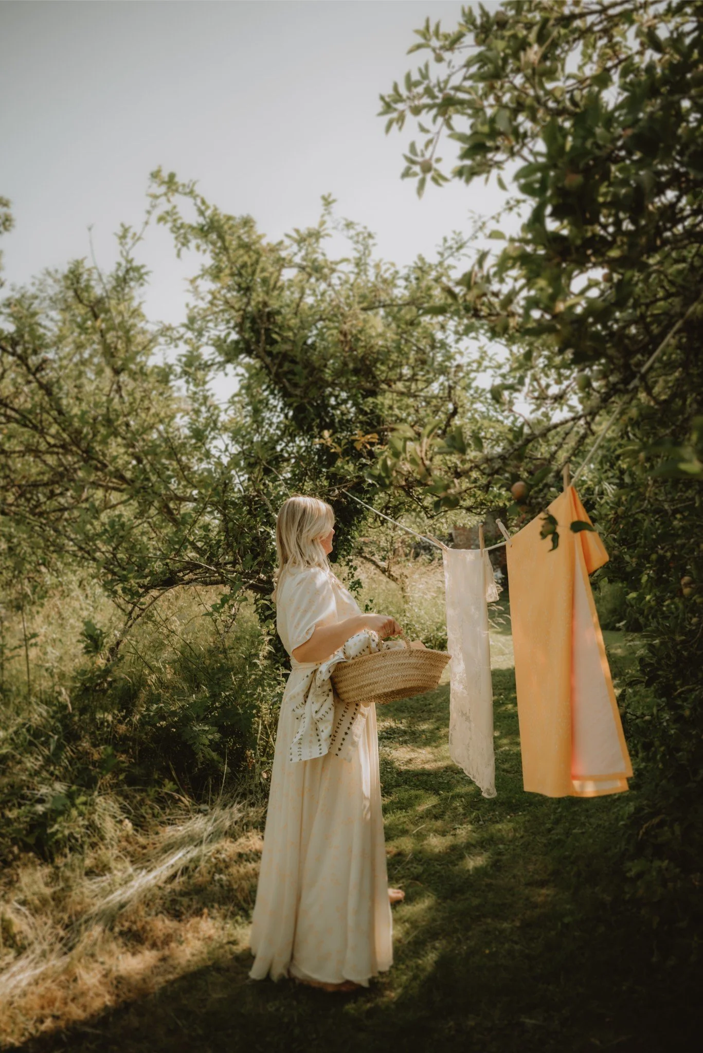 A woman hanging laundry on a clothesline in a lush garden.