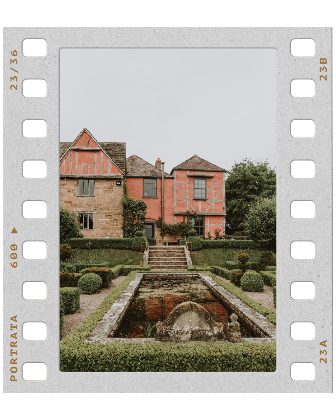 A historic building with a garden and fountain in front, featuring a combination of beige stone and red brick with timber framing, surrounded by greenery.