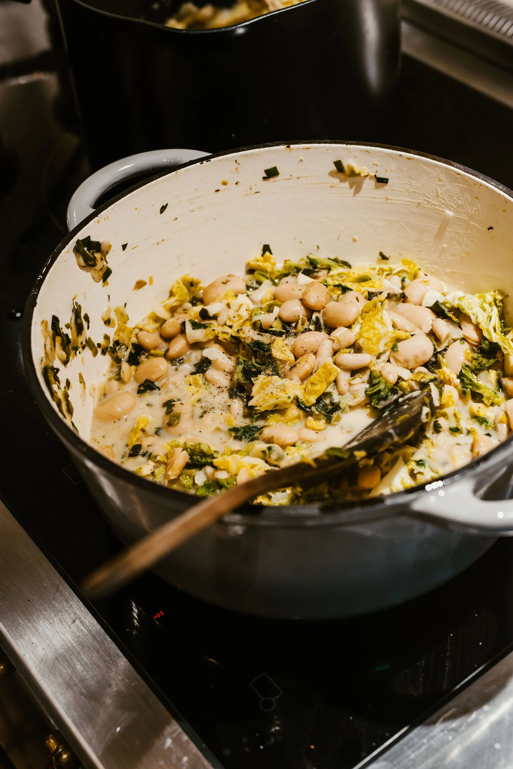 A pot with white bean and vegetable stew cooking on an electric stove.