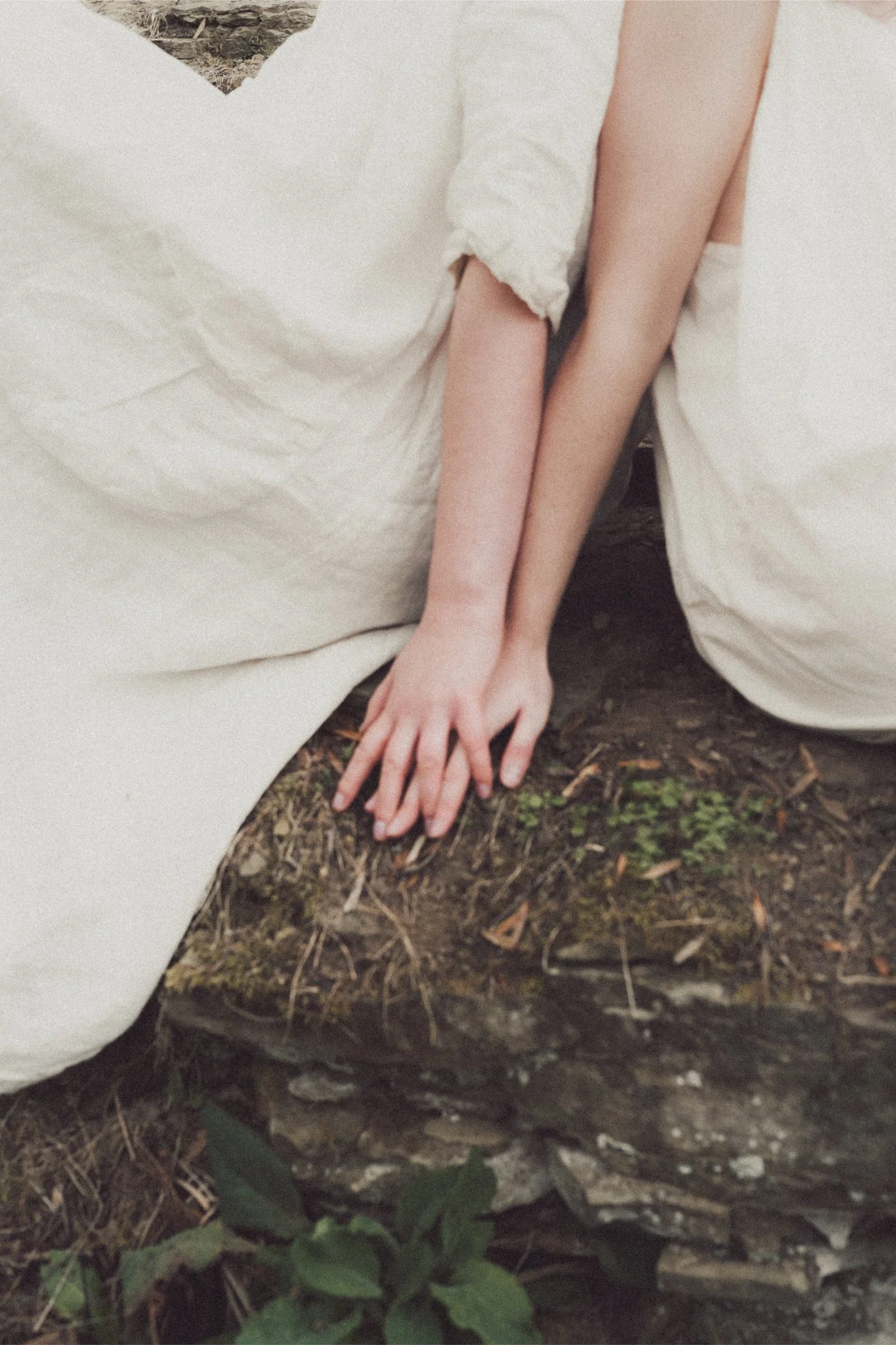 A person in a white dress sitting on a rock with their hand resting on the ground.