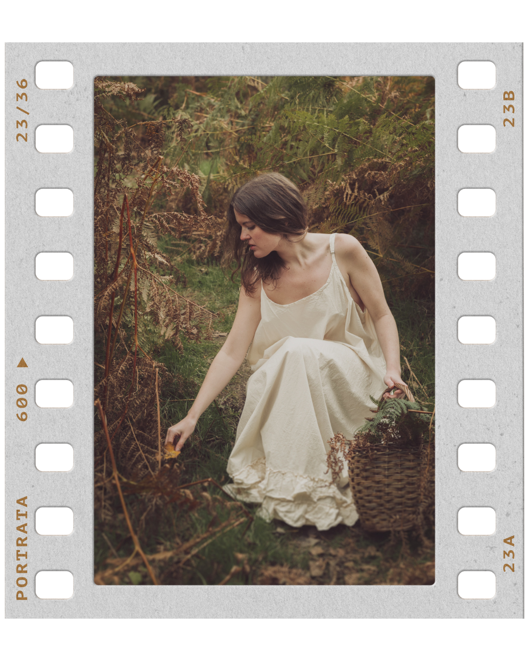 A woman in a beige dress sitting outdoors among ferns and dried foliage, reaching down toward the ground with a basket beside her.