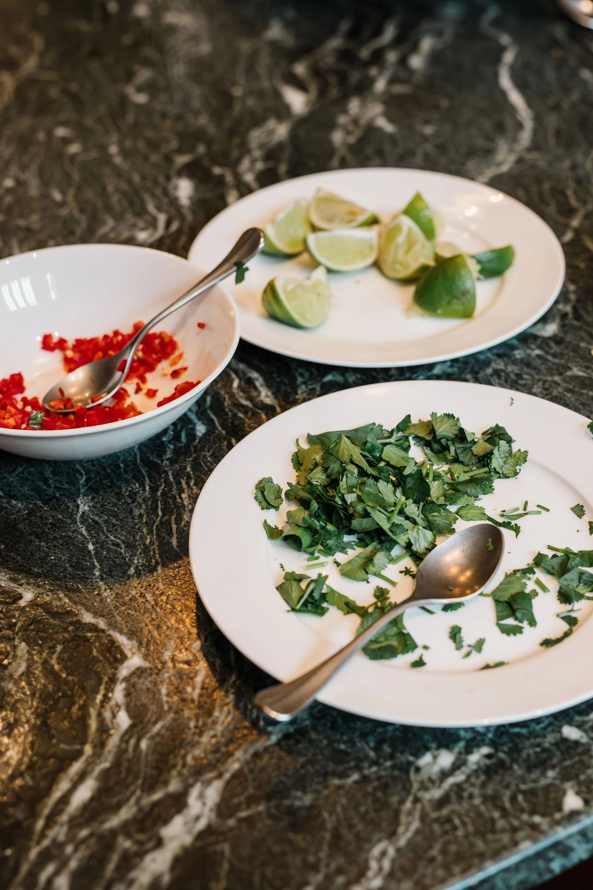 Three plates with lime wedges, chopped red peppers, and chopped cilantro on a dark marbled countertop.
