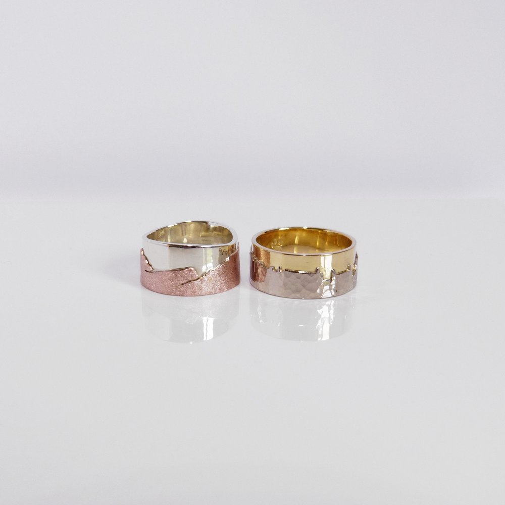 9ct white and red gold landscape ring sitting next to an 18ct white and yellow gold landscape ring. The red and white is polished and textured. The yellow and white ring is polished and hammered.