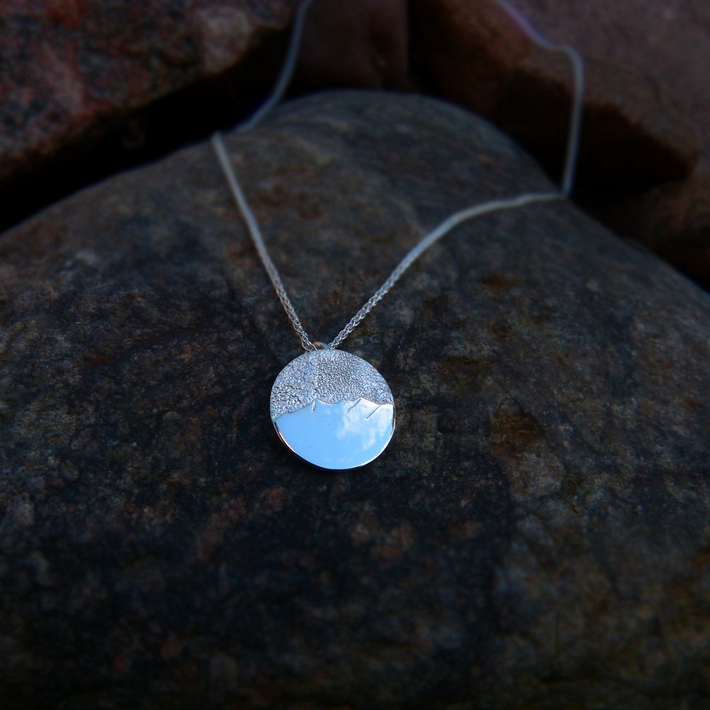 A circular silver pendant featuring the Cullin, resting on a rock.