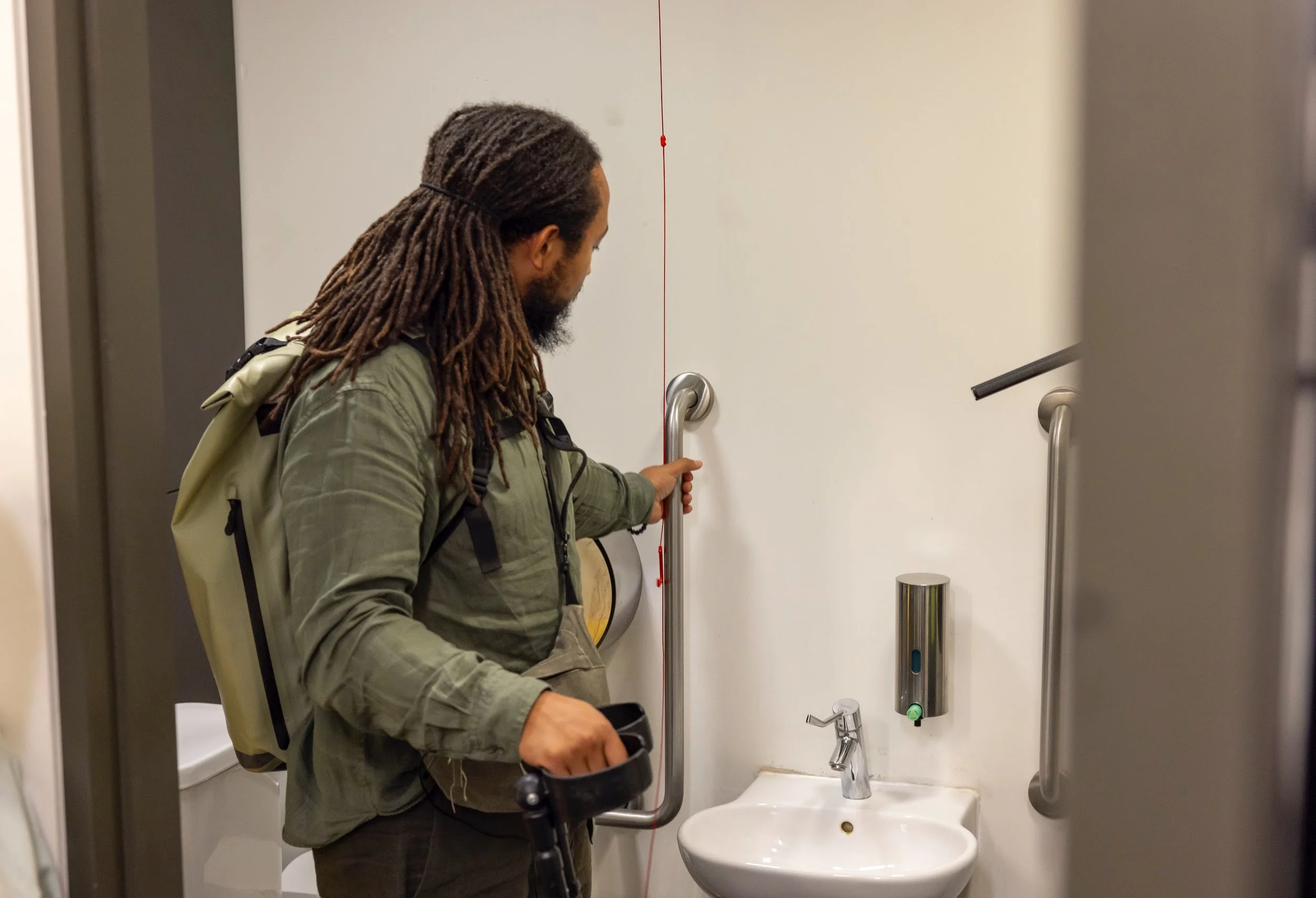 A black man using crutches reaching out to the handrails in a toilet setting, near the sink.