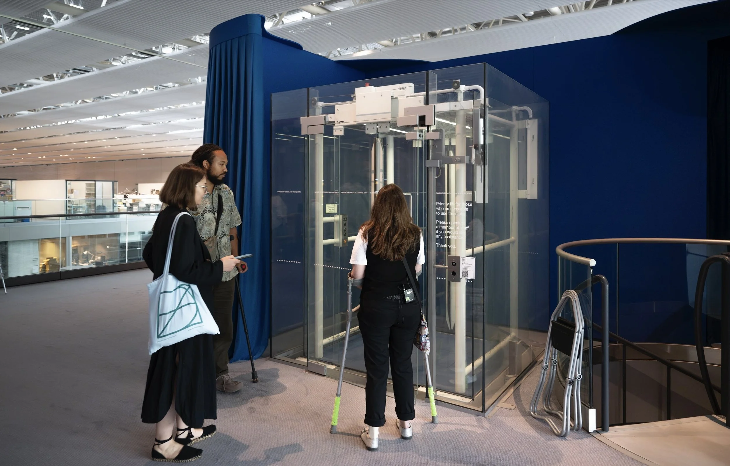 Group of three people near a clear lift reading the text on the lift. 