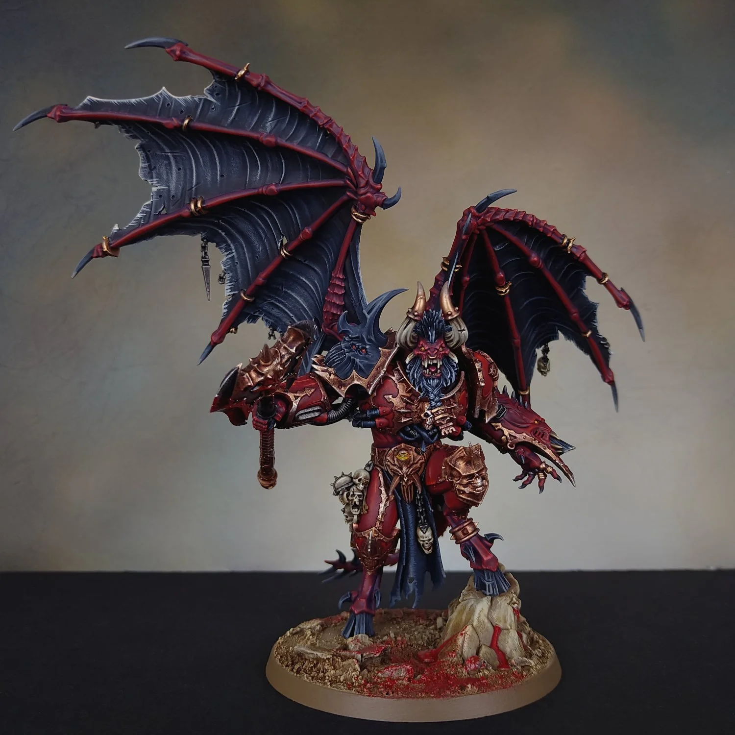A detailed painted miniature figure of a demonic warrior with large black and red wings, wearing skull-adorned armor and holding a weapon, standing on a textured base.