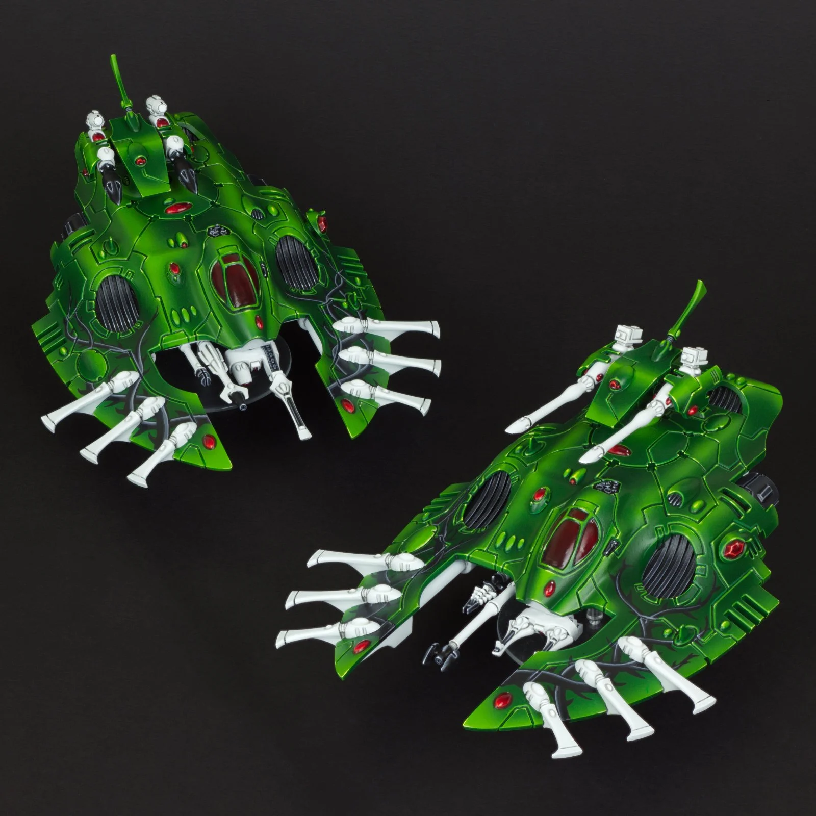 Two green toy robotic spider-like vehicles with white legs and red accents, set against a black background.