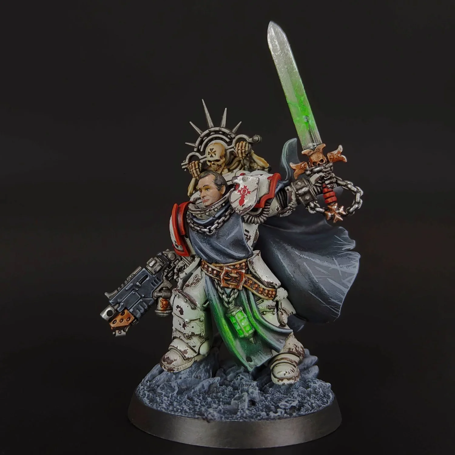 A detailed miniature figure of a space marine from Warhammer 40K, wielding a gun in one hand and a glowing green sword in the other, standing on a rocky base with a dark background.