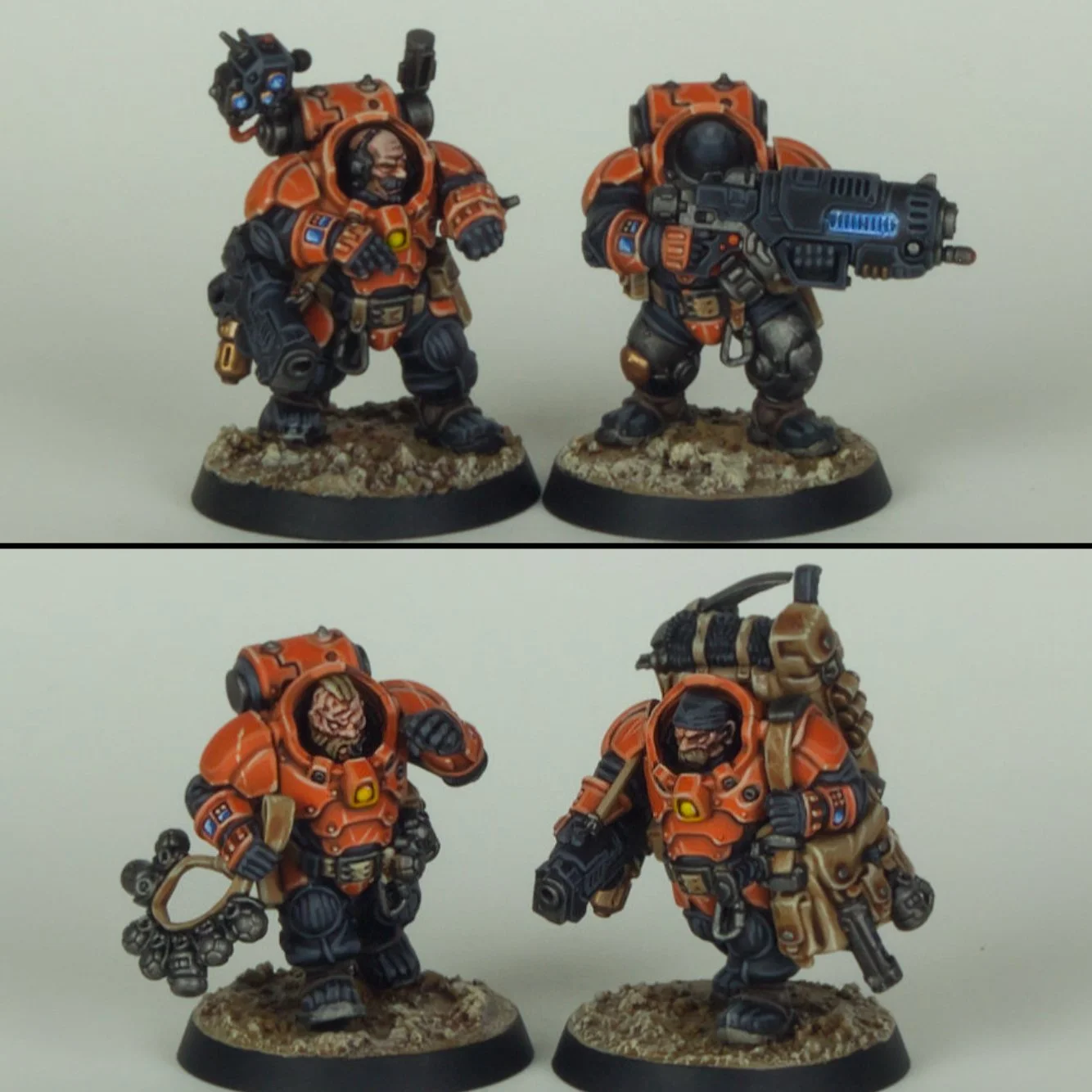 Four painted miniature figures of armored soldiers, two holding guns, one with a backpack and a coil of cable, all standing on bases with rocky terrain.