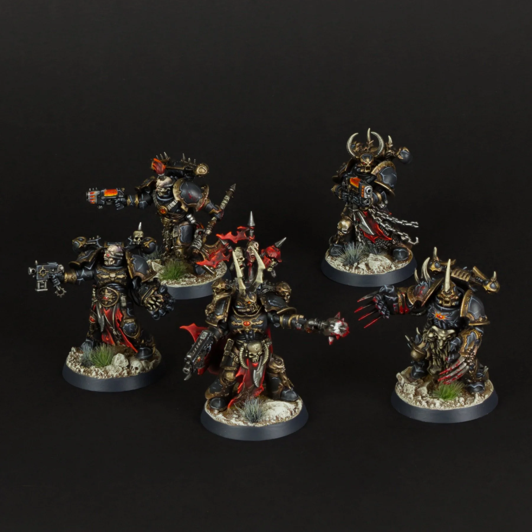 Group of detailed miniature figurines of heavily armored warriors with skull motifs, chains, weapons, and elaborate armor, set on bases with rocks and grass, against a black background.