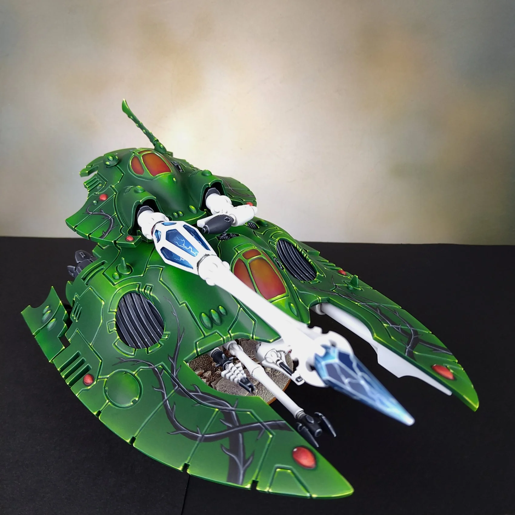 A model spaceship with a sleek green and black design, painted with circuit-like lines and red accents, positioned on a black surface.